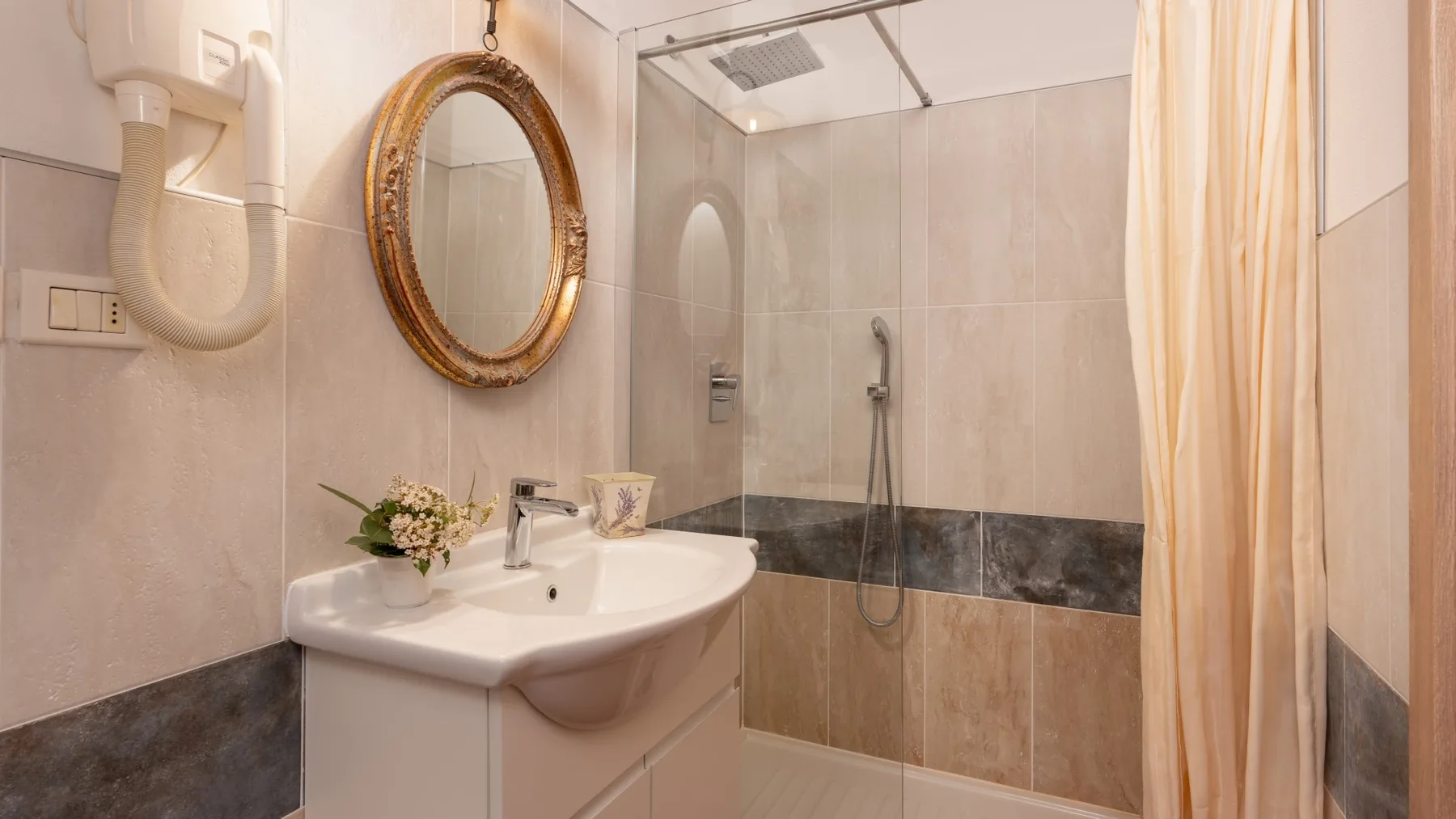 A tiled bathroom with a sink, oval mirror, and shower behind a curtain.