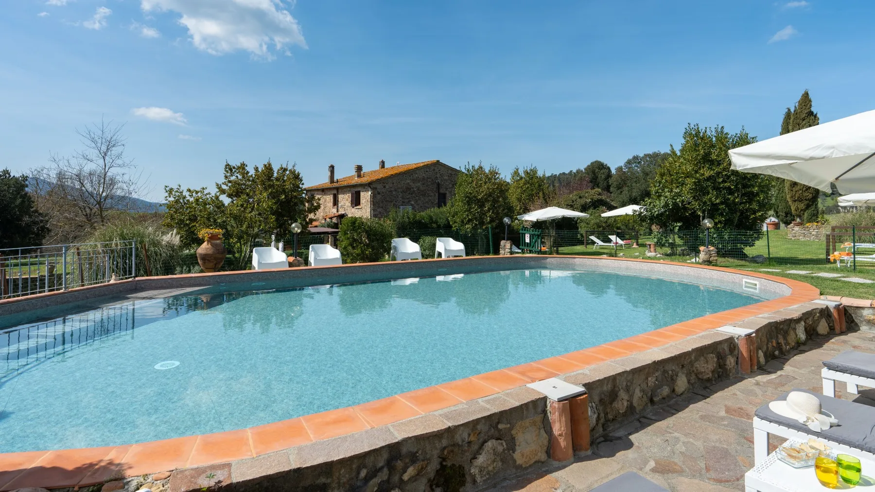 An outdoor swimming pool bordered by terracotta-colored tiles, with greenery and hills beyond.