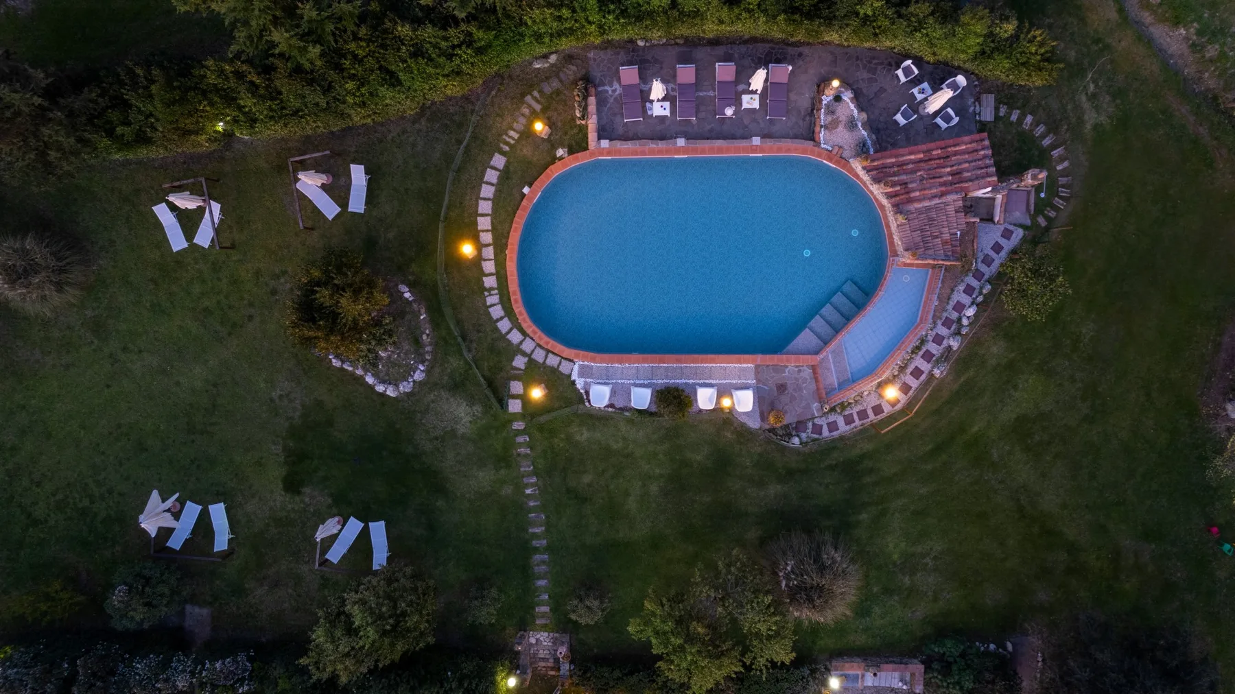 An aerial view of an outdoor swimming pool surrounded by greenery and seating.