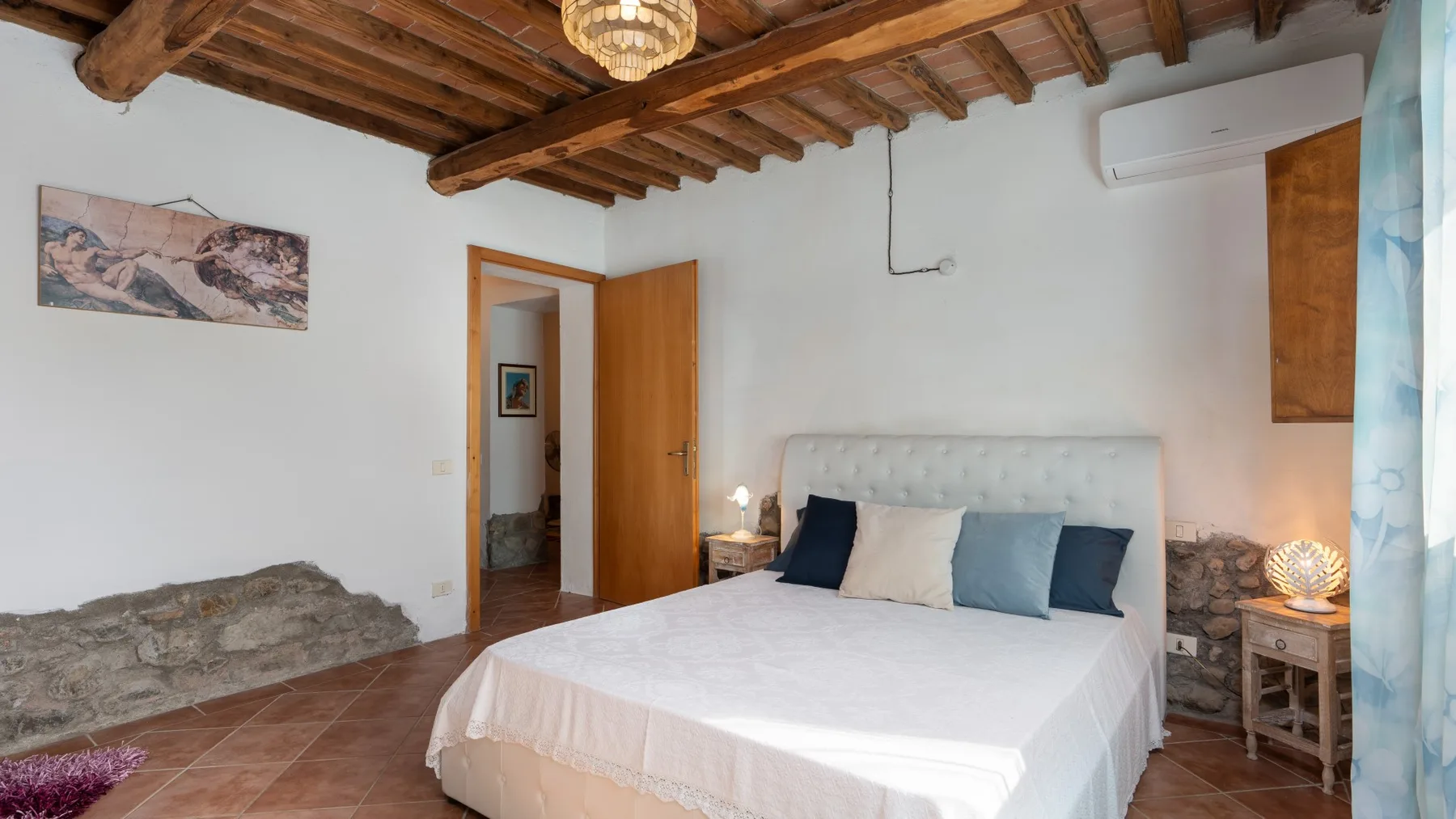 A bedroom with a large bed, exposed wooden ceiling beams, and an open doorway.