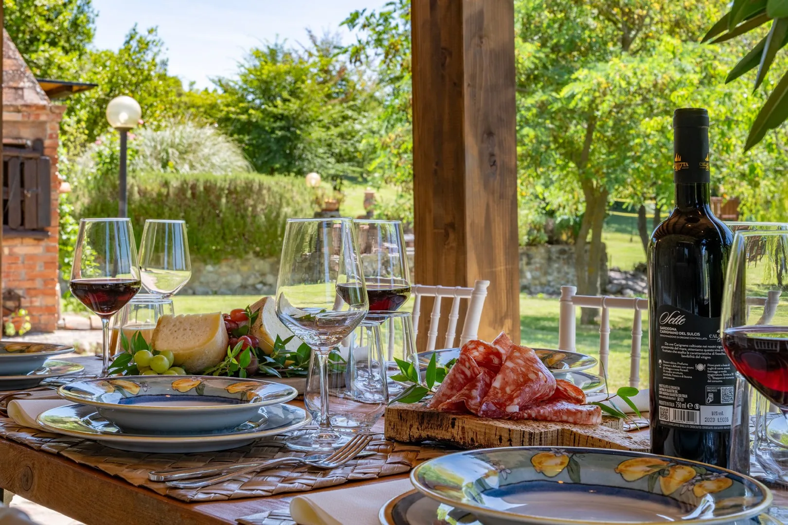 An outdoor dining table is set with wine glasses, plates, and food.