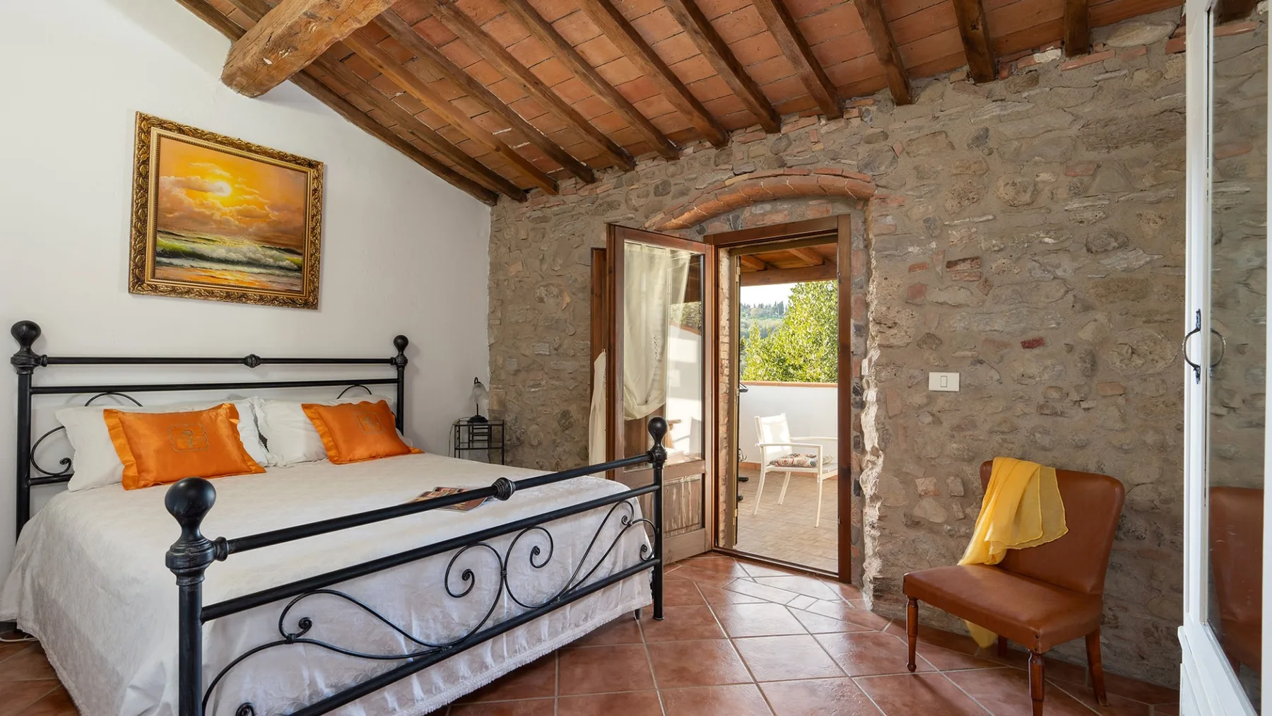 A bedroom with a metal bed, exposed wooden ceiling beams, and a stone doorway.