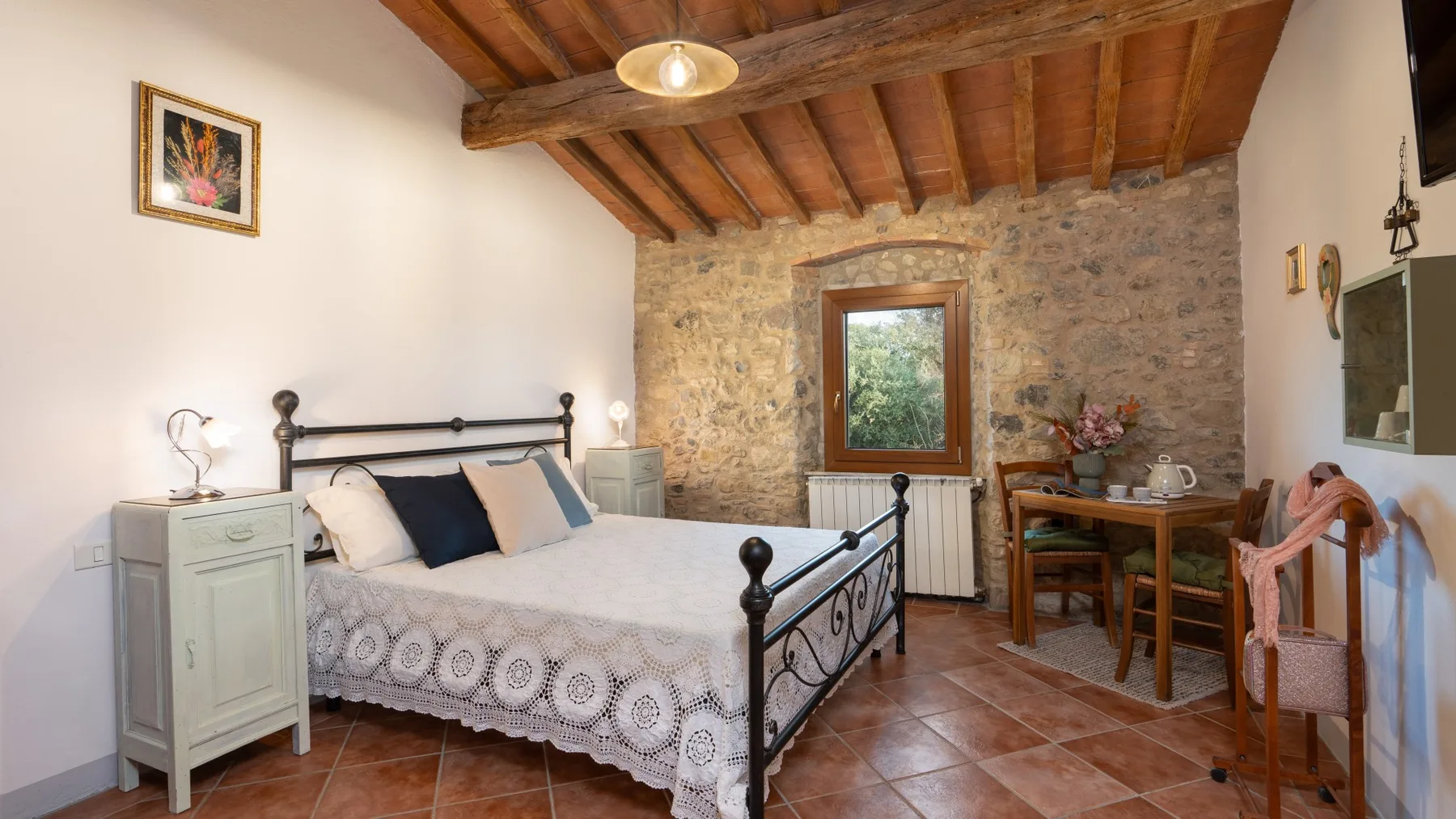 A bedroom with a bed, exposed wooden ceiling beams, and a small table by the window.