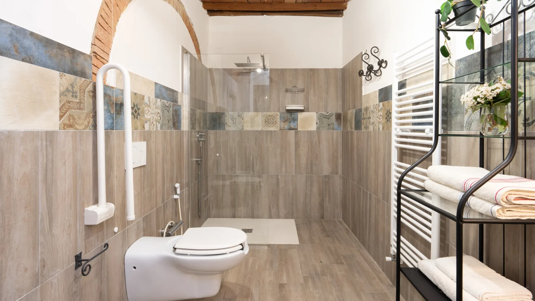 A tiled bathroom with a toilet, glass shower, and towel rack.