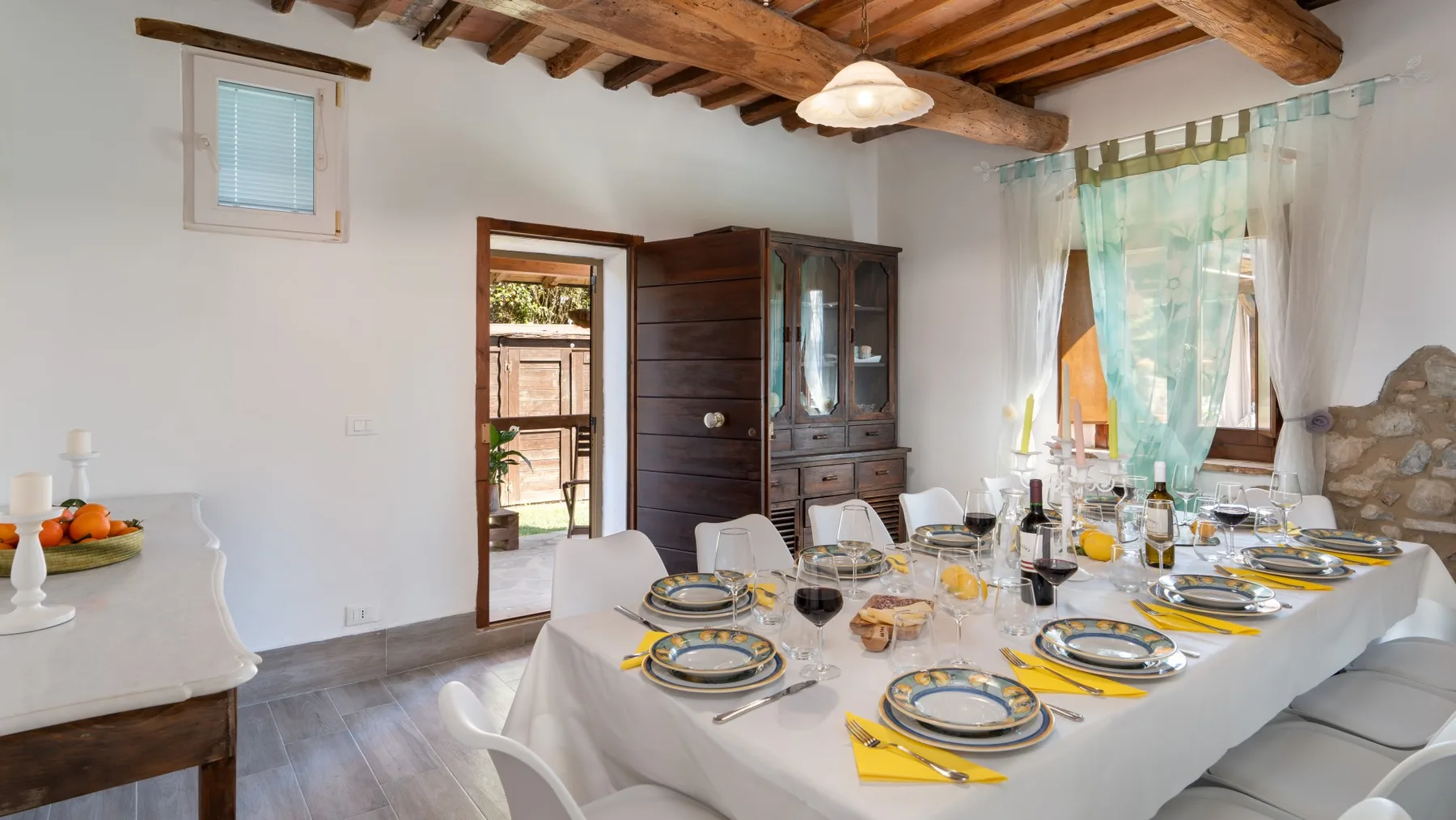A dining room with a long table set with plates and glassware beneath exposed wooden beams.