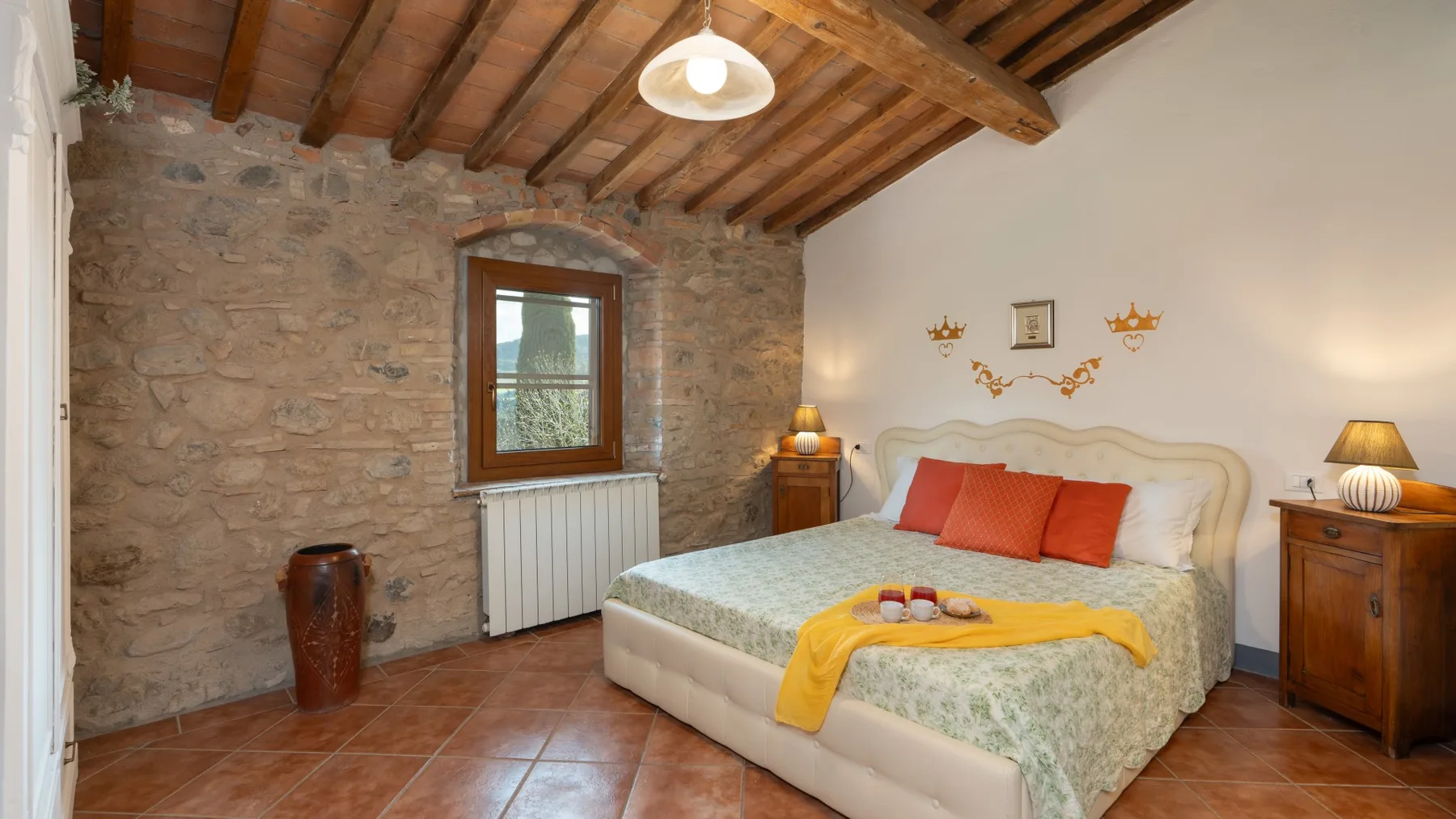 A bedroom with a bed, exposed wooden ceiling beams, and a stone wall.