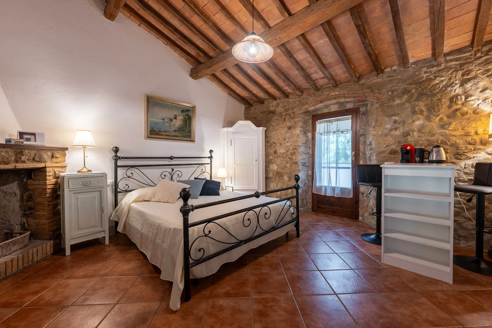 A bedroom with a wrought-iron bed, stone wall, and exposed wooden ceiling beams.