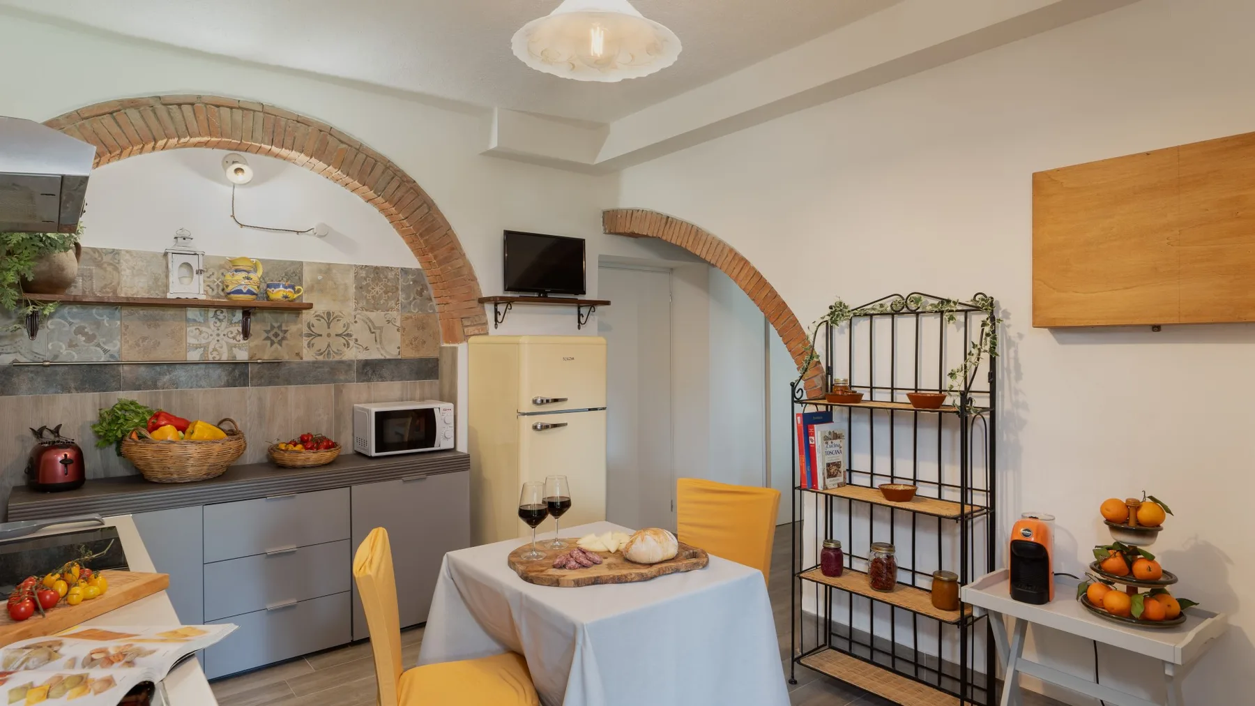 A dining area with a table set with bread and fruit beside a kitchen counter.