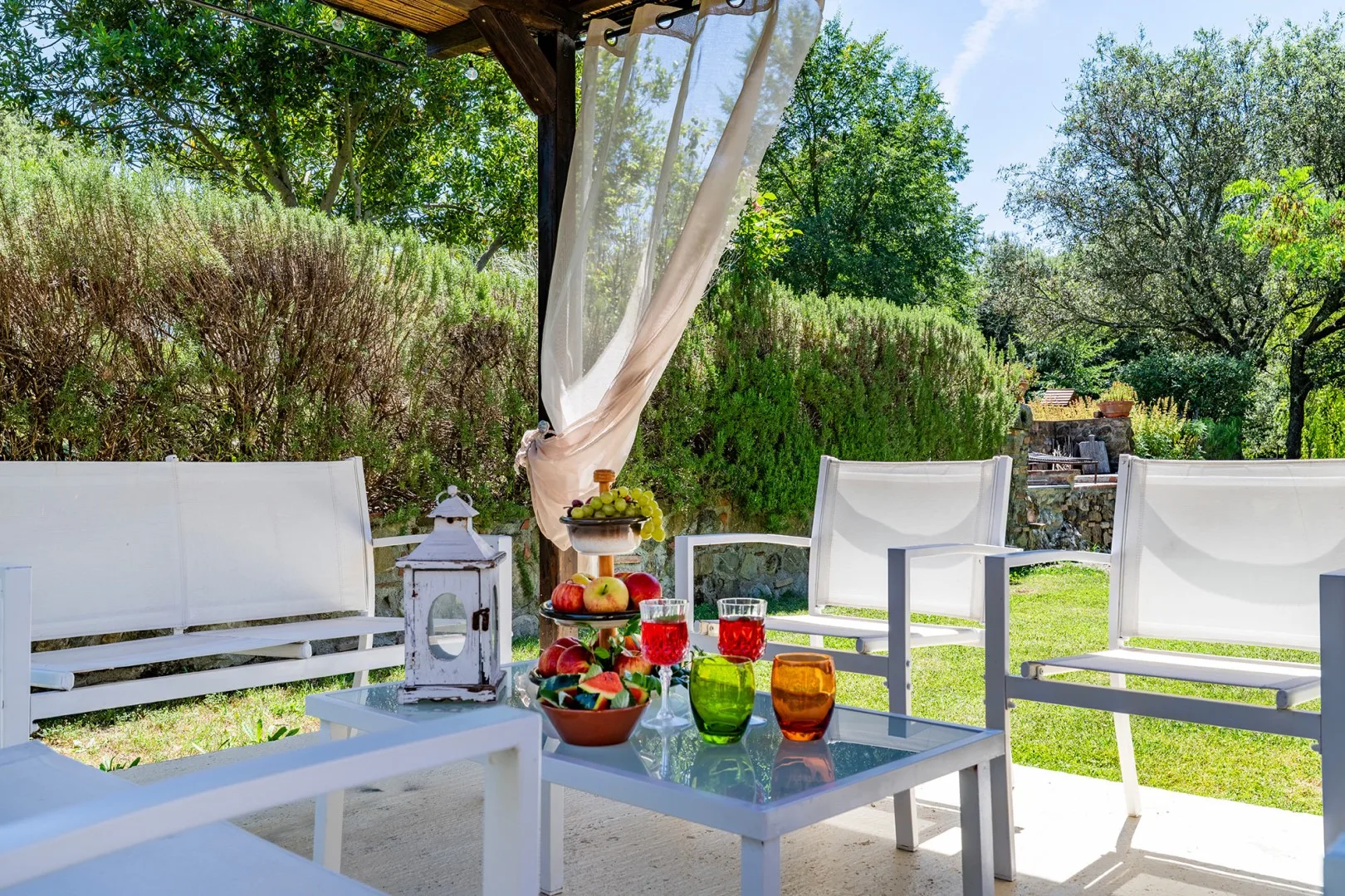 An outdoor seating area with white chairs and a table beneath a shaded pergola.