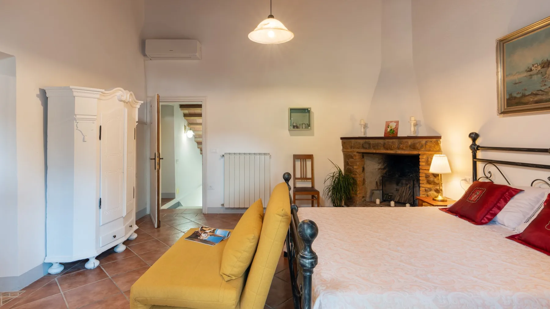 A bedroom with a large bed, yellow seating, and a fireplace.