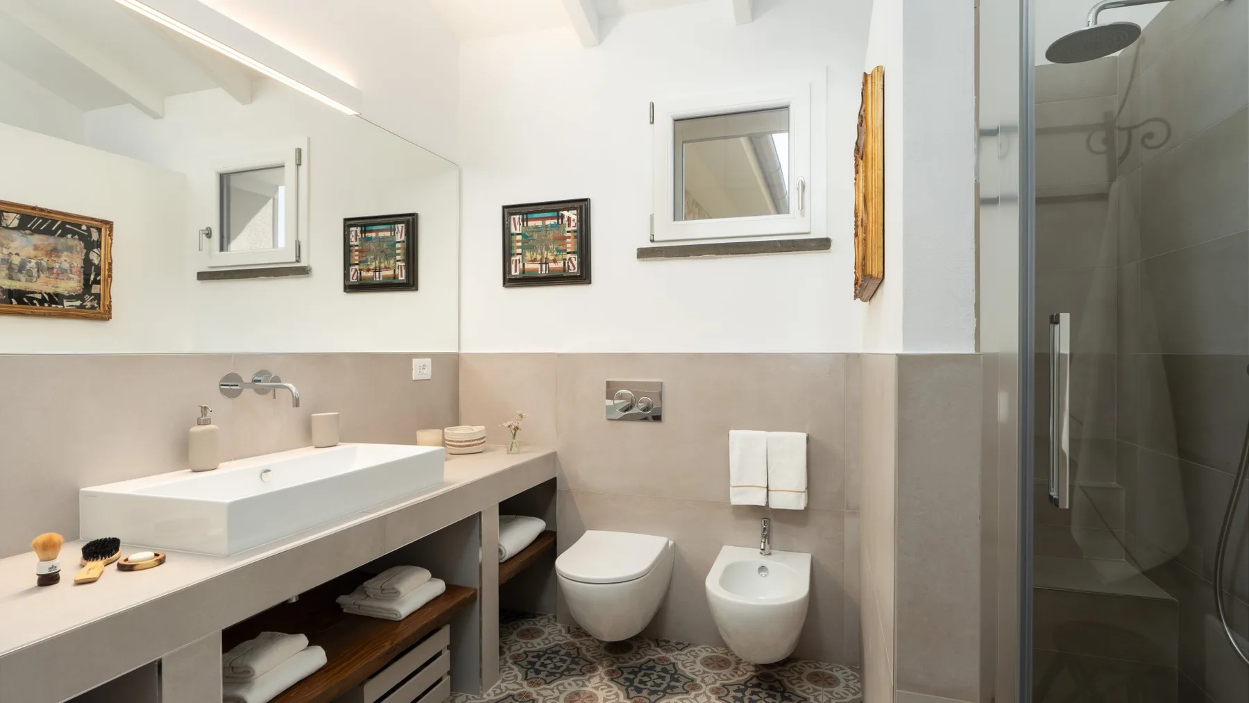 A bathroom with a long sink counter, toilet, bidet, and glass shower.