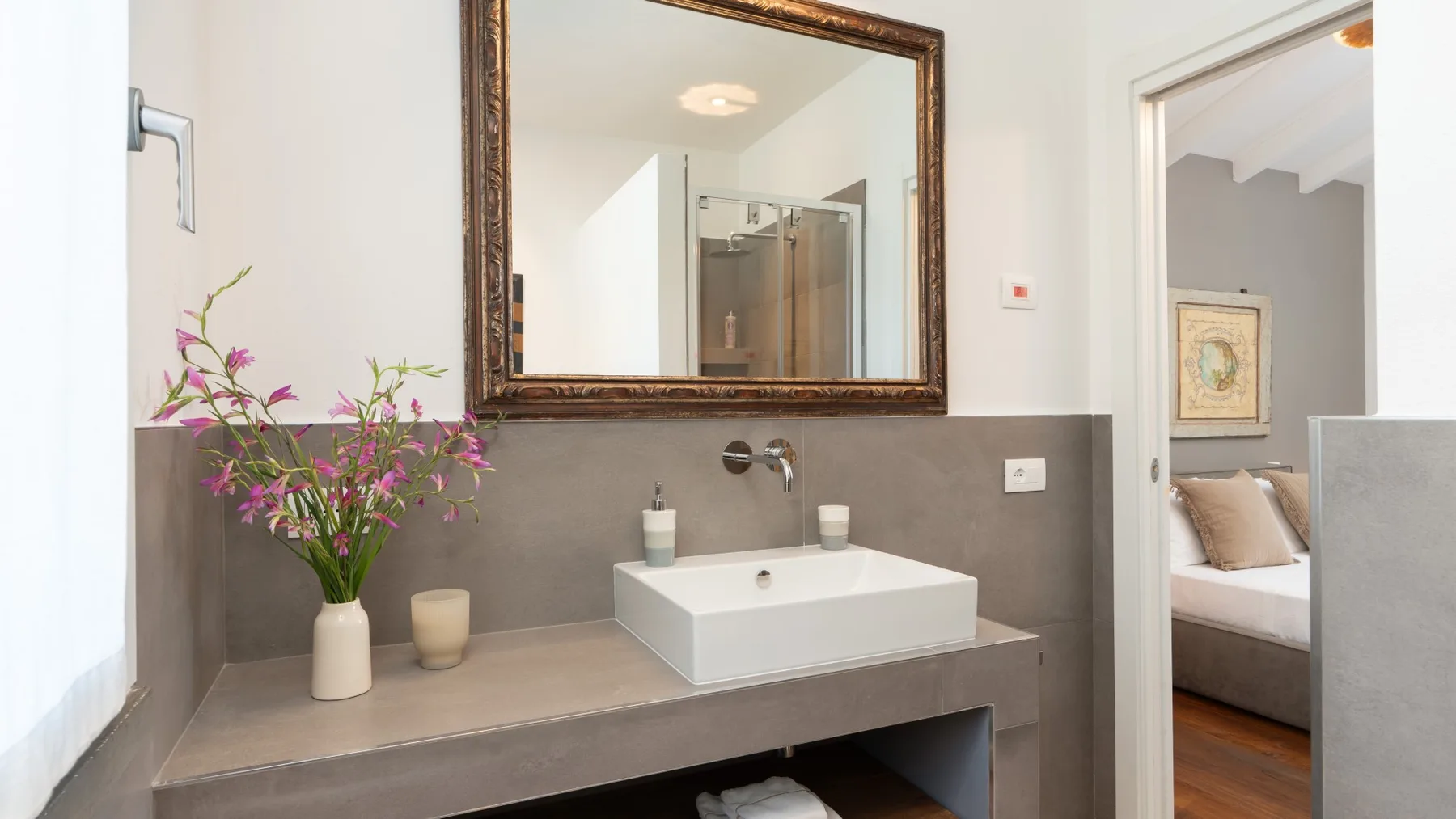 A bathroom vanity with a wall mirror and flowers beside the sink.