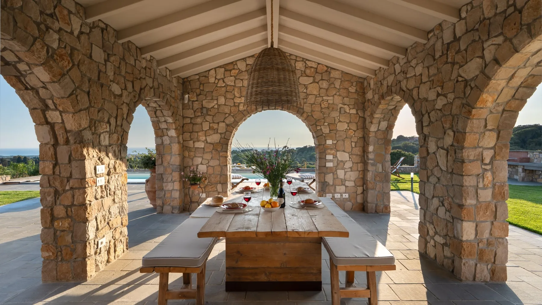 A stone patio dining area with a long table set beneath arched openings.
