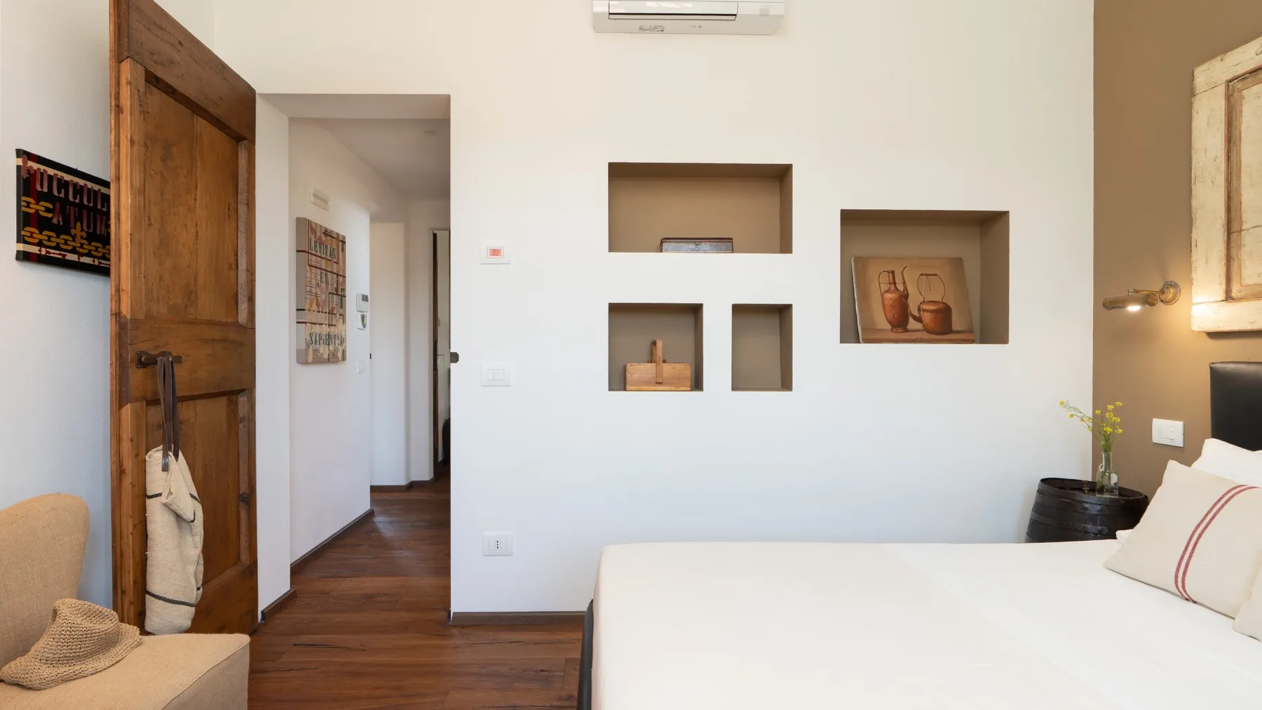 A bedroom with a large bed, wooden flooring, and recessed wall shelves.