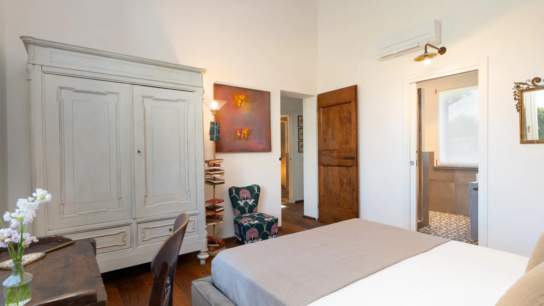 A bedroom with a large bed, painted wardrobe, and a doorway to the bathroom.