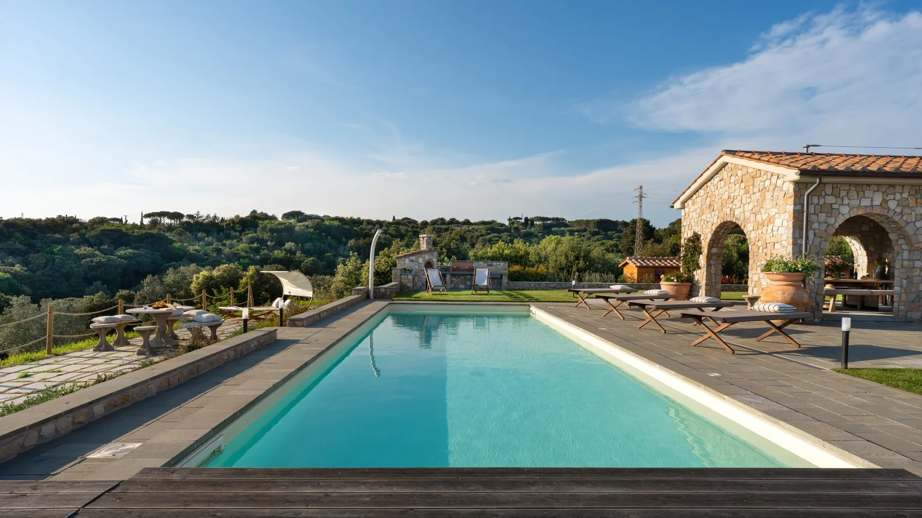 An outdoor swimming pool sits beside a stone building and paved terrace.