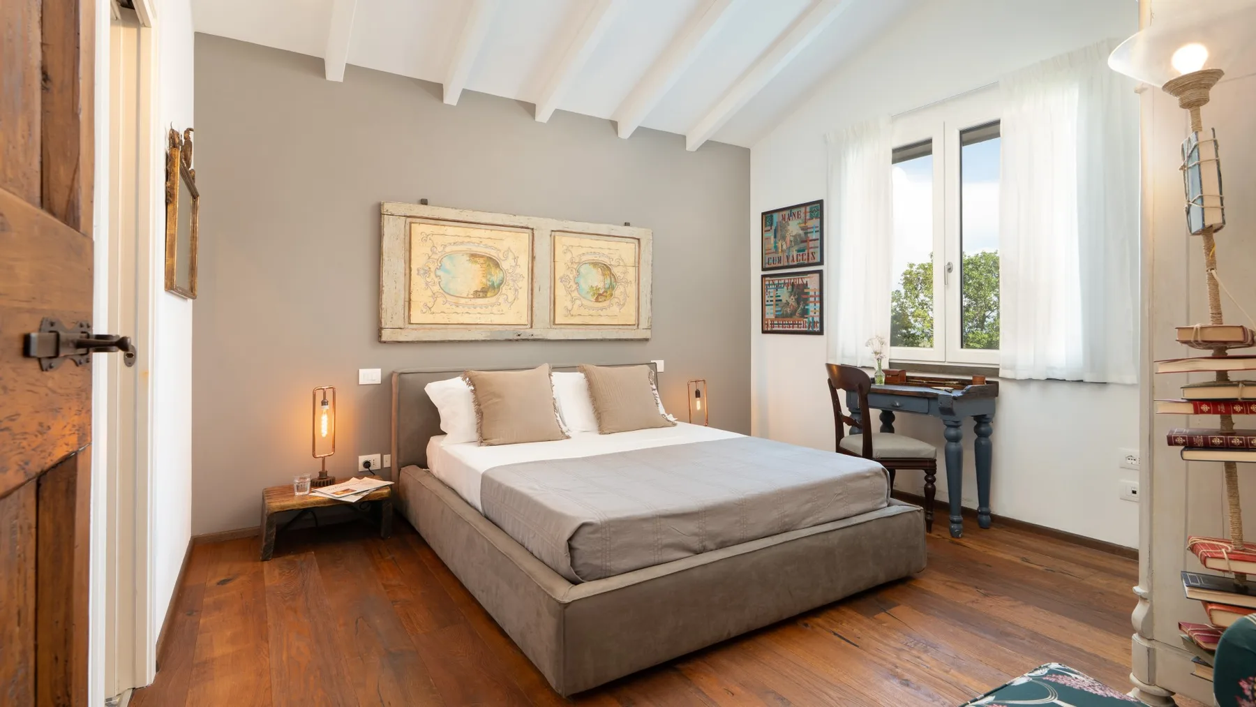 A bright bedroom with a large bed, wooden flooring, and tall windows.