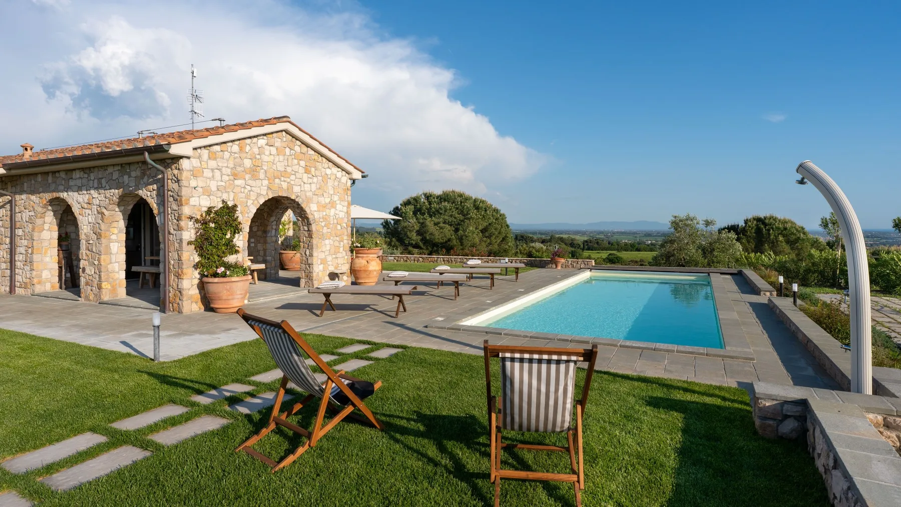 A stone building stands beside a swimming pool, with lawn and outdoor seating.