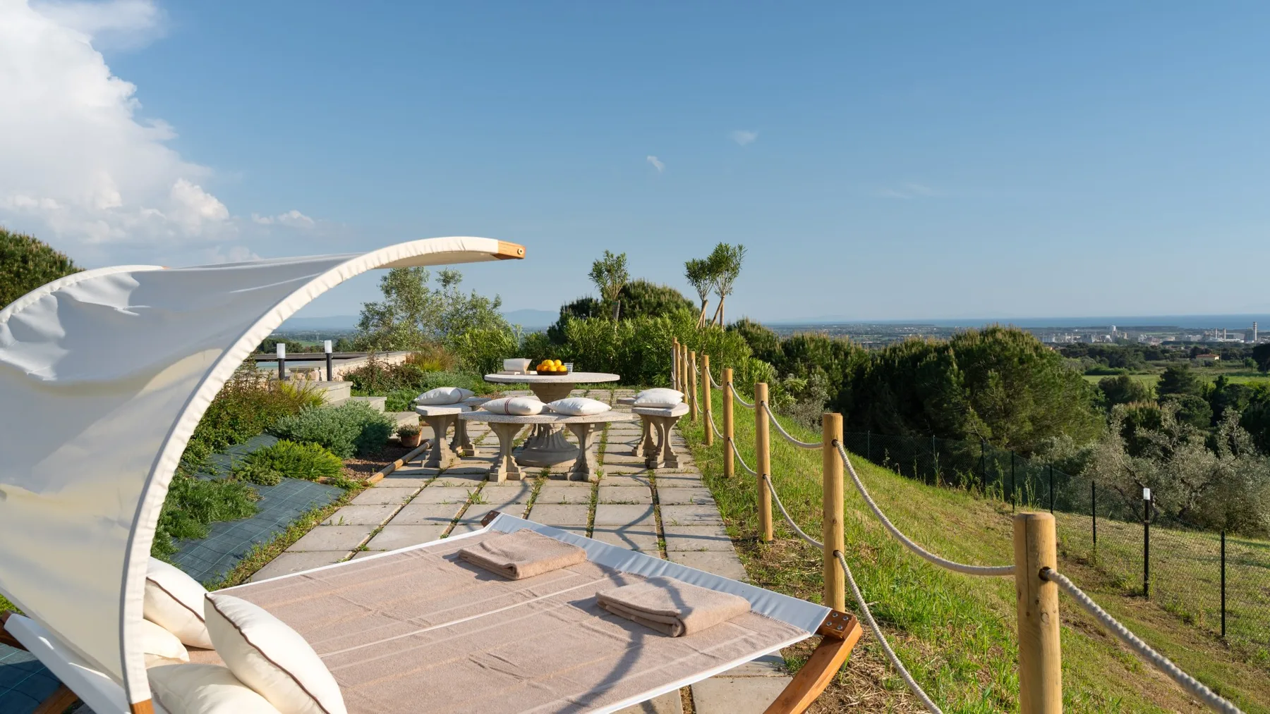 An outdoor terrace with a dining table and seating overlooks a green landscape.