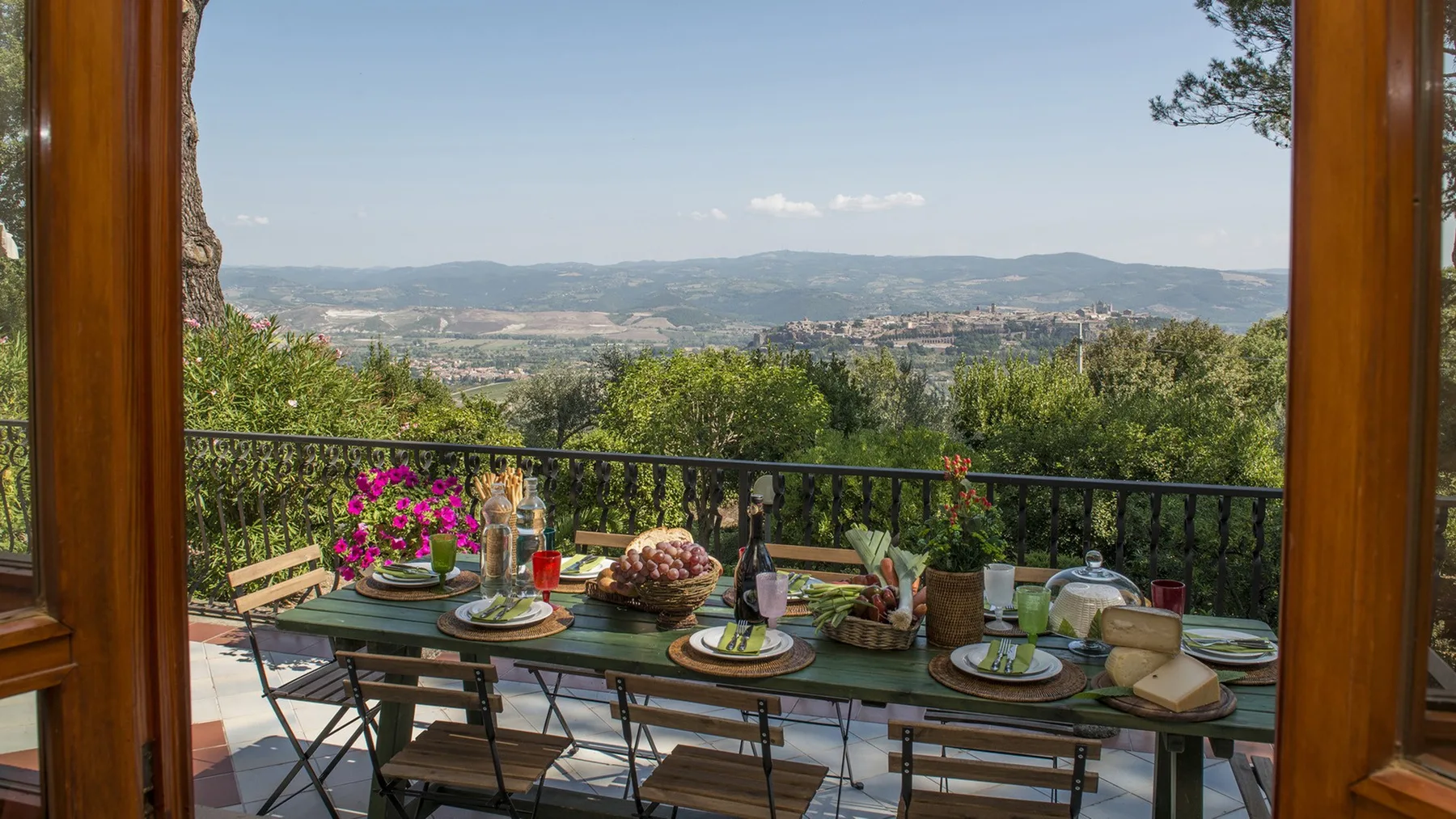 Una mesa exterior preparada para comer mira a un valle verde y colinas lejanas a través de una puerta abierta.