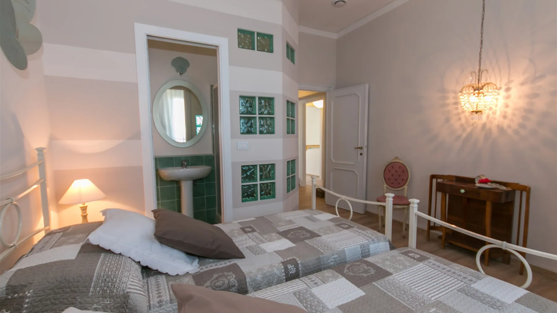 Un dormitorio con una cama de estructura metálica, una lámpara de mesilla y un lavabo alicatado junto a la puerta abierta.