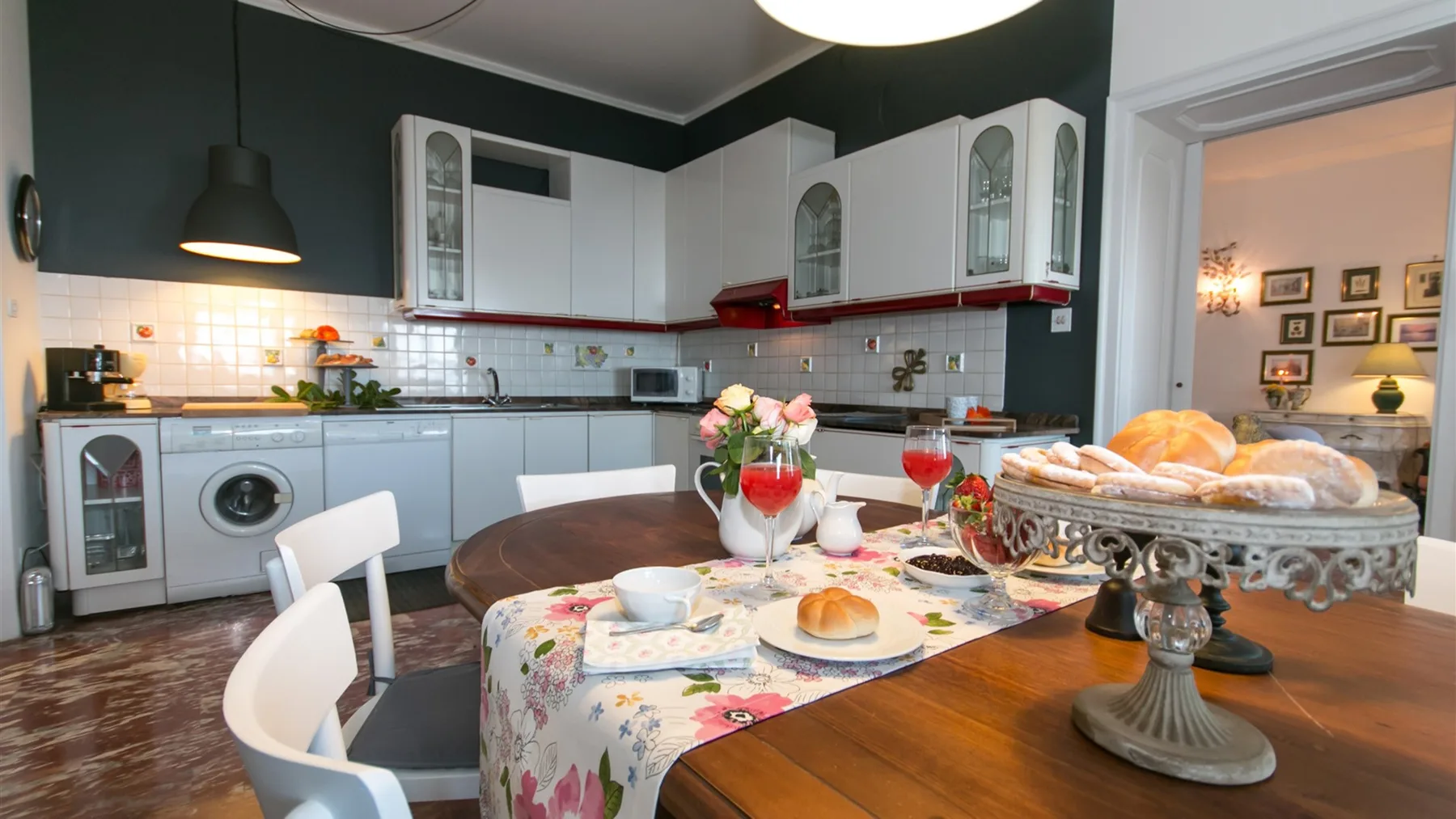 Una cocina con zona de comedor, gabinetes blancos, electrodomésticos de lavandería y una mesa puesta con comida y flores.