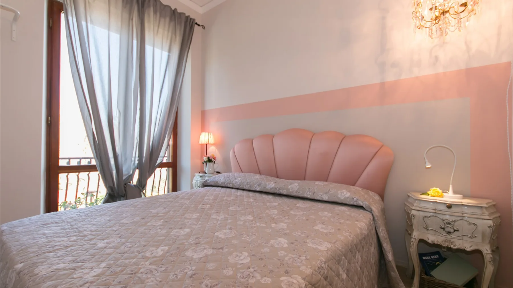 Un dormitorio con una cama grande, una ventana alta con cortinas y una mesita de noche.