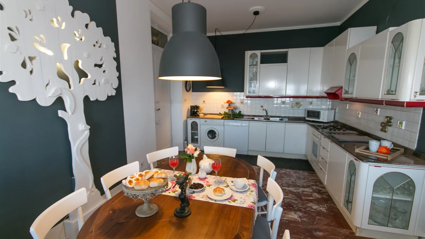 Una cocina en forma de U tiene armarios blancos, una lavadora y una mesa puesta con platos y fruta.