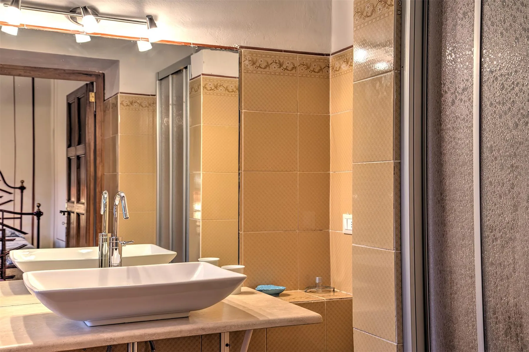 Un baño alicatado tiene dos lavabos blancos sobre una encimera de piedra junto a una mampara de ducha de vidrio.