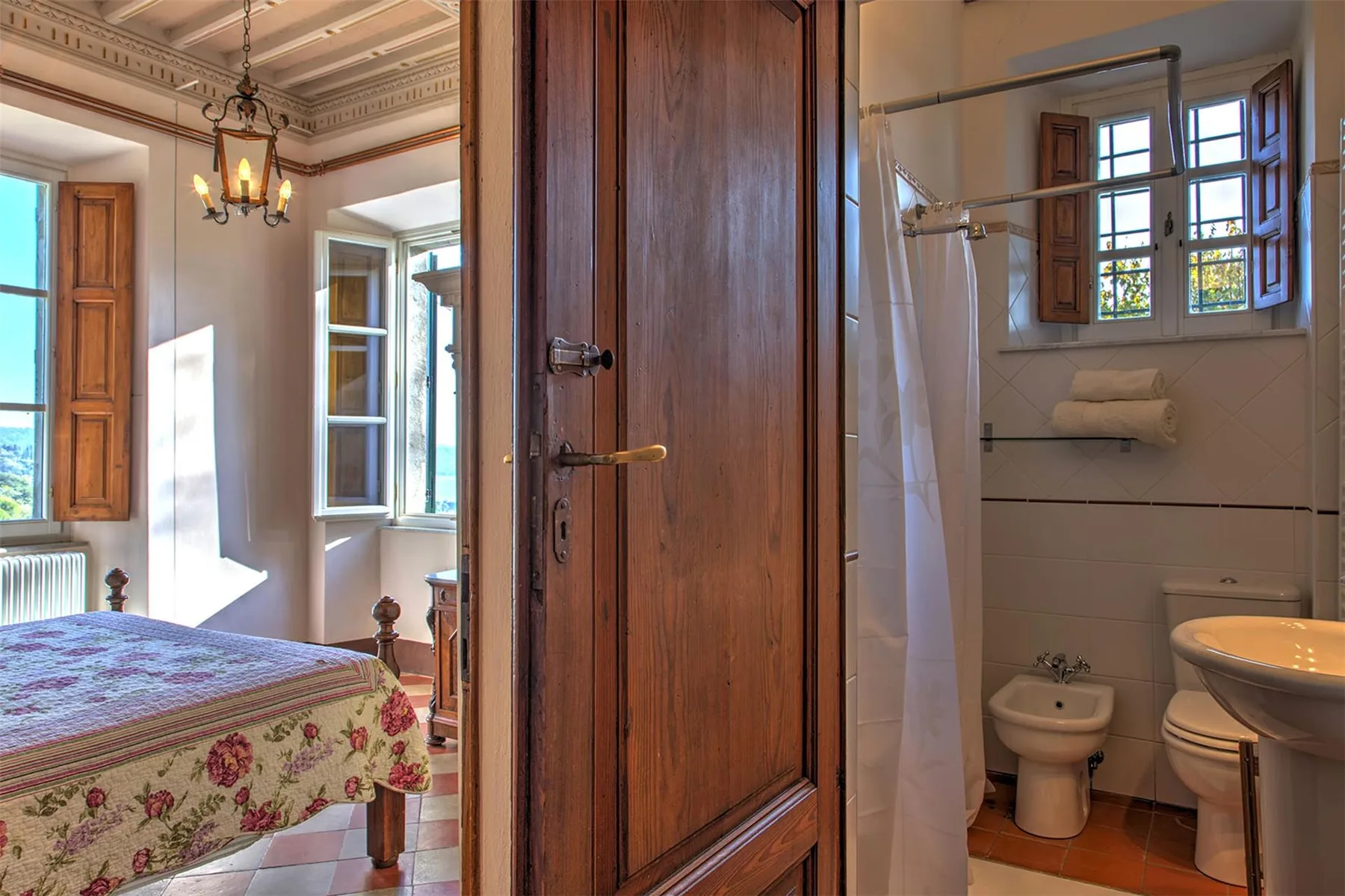 Se ve un dormitorio con una colcha floral junto a un baño con bañera, inodoro y bidé.