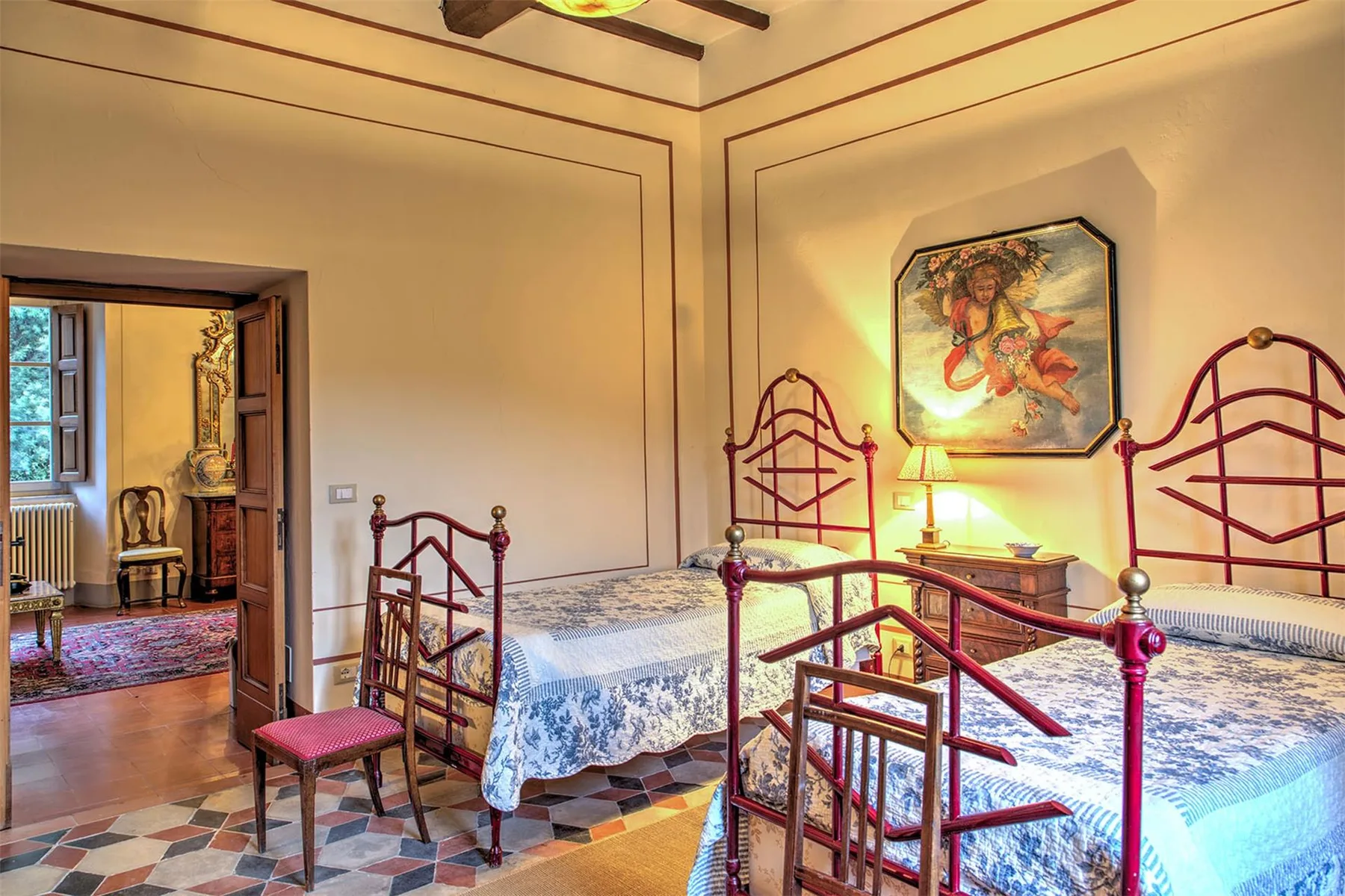 Un dormitorio con dos camas individuales, armazones rojos de metal, colchas estampadas y un cuadro enmarcado.