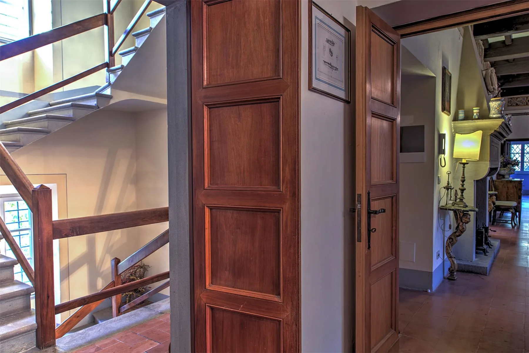 Pasillo interior con una escalera de madera, puertas con paneles y una lámpara encendida.