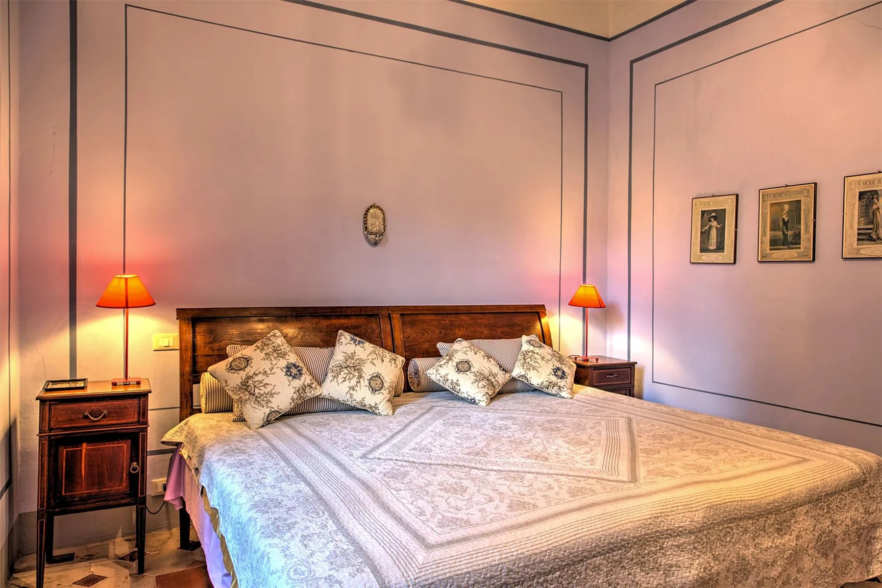 Dormitorio con una cama grande, ropa de cama estampada, mesillas a juego y lámparas cálidas.