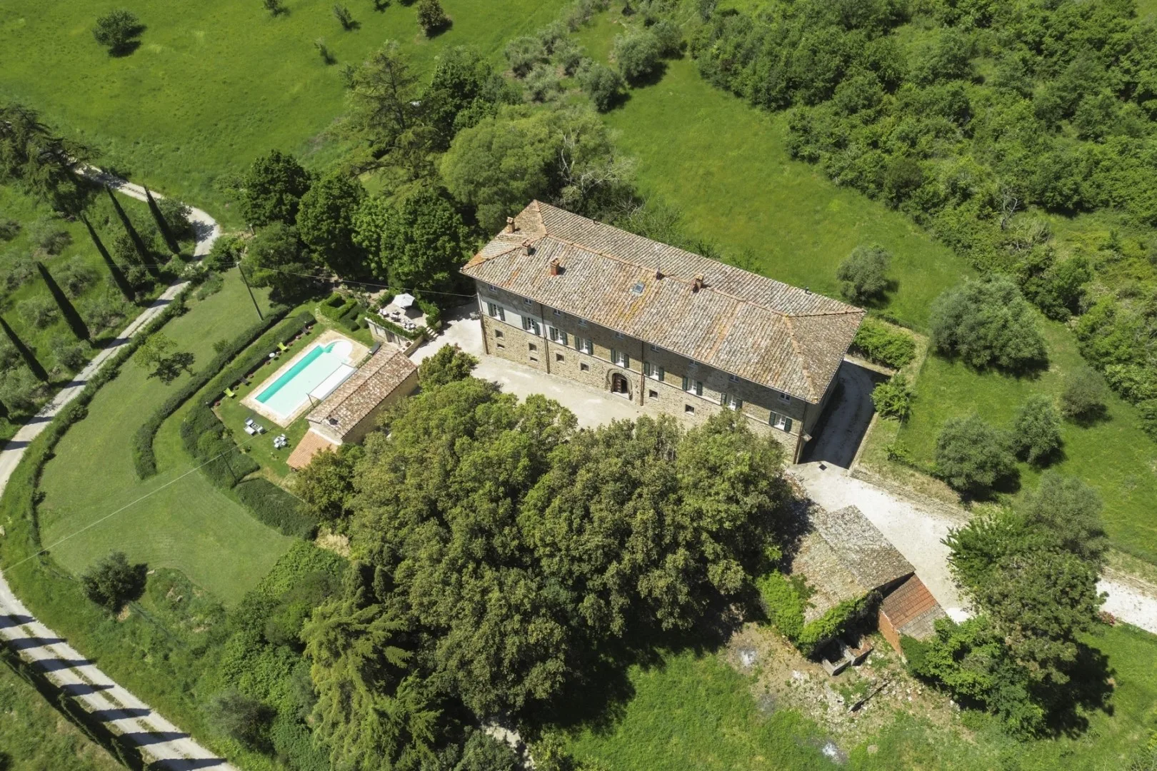 Vista aérea de una casa de piedra con tejado de tejas, rodeada de zonas verdes y una piscina.