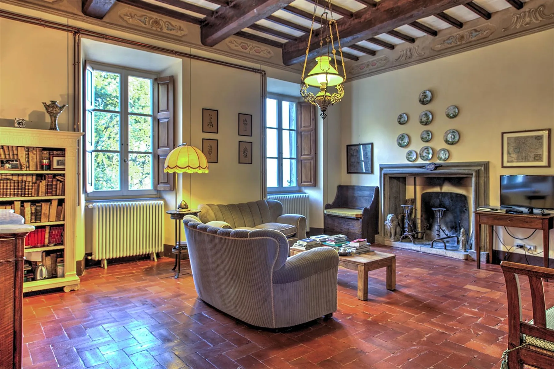 Una sala de estar tradicional con una gran chimenea, sillones tapizados, estanterías y vigas de techo a la vista.