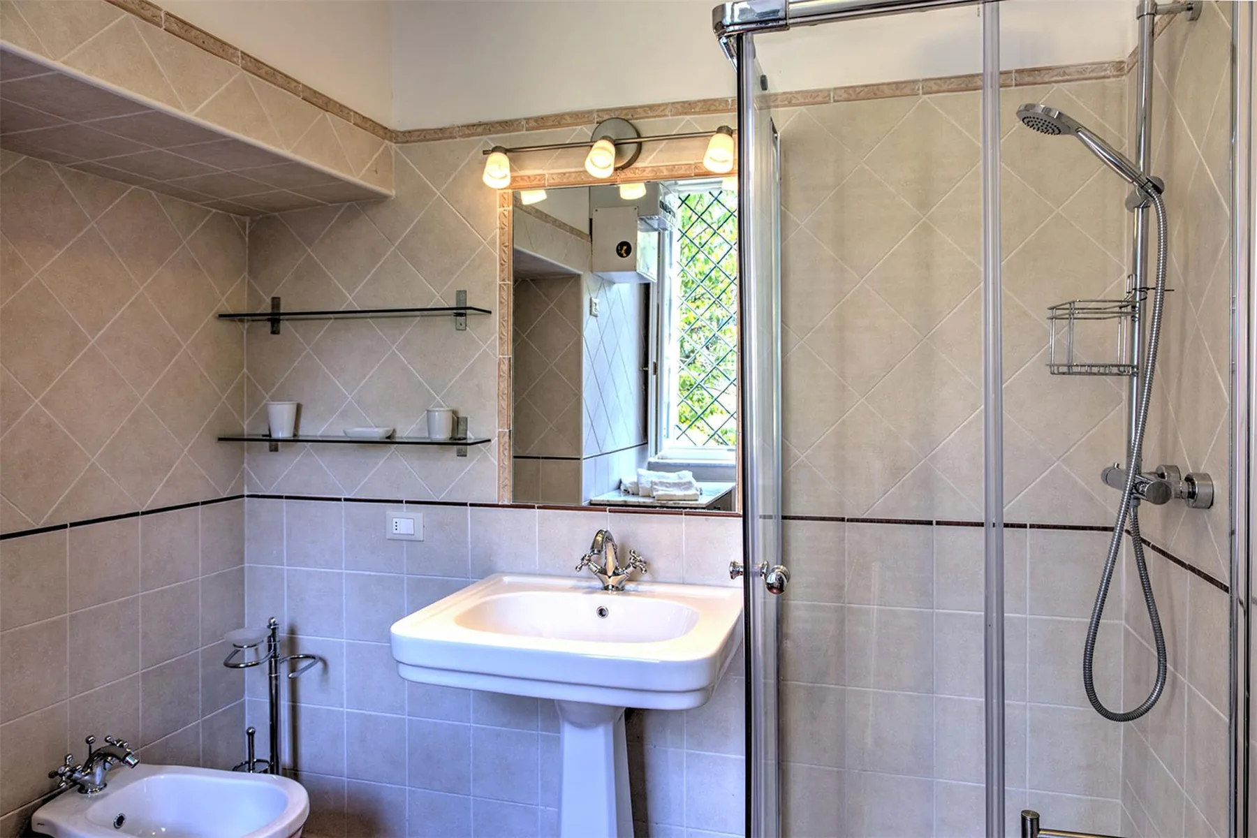 Un baño alicatado con lavabo de pedestal, espejo de pared, mampara de ducha y bidé.