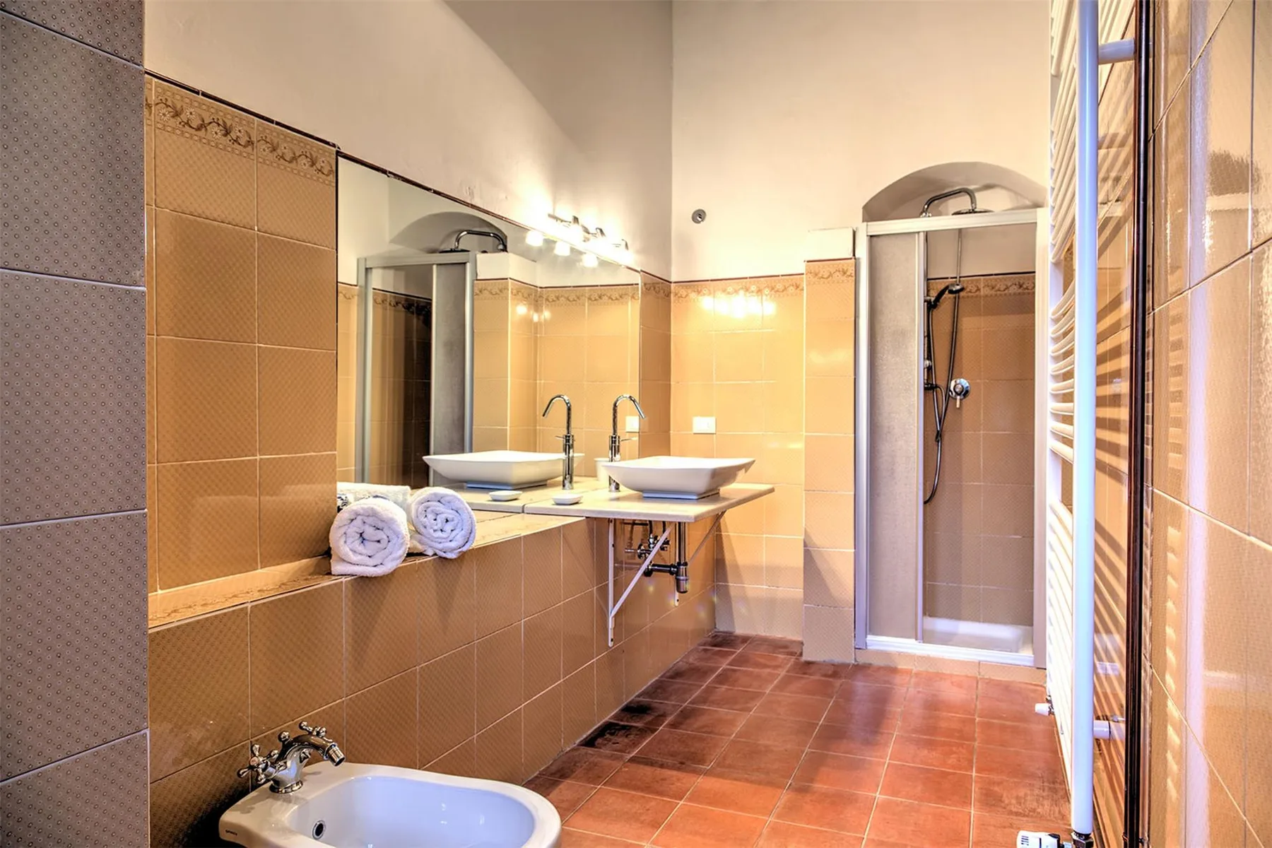 Un baño alicatado tiene dos lavabos sobre encimera, una bañera y una ducha con mampara de vidrio.