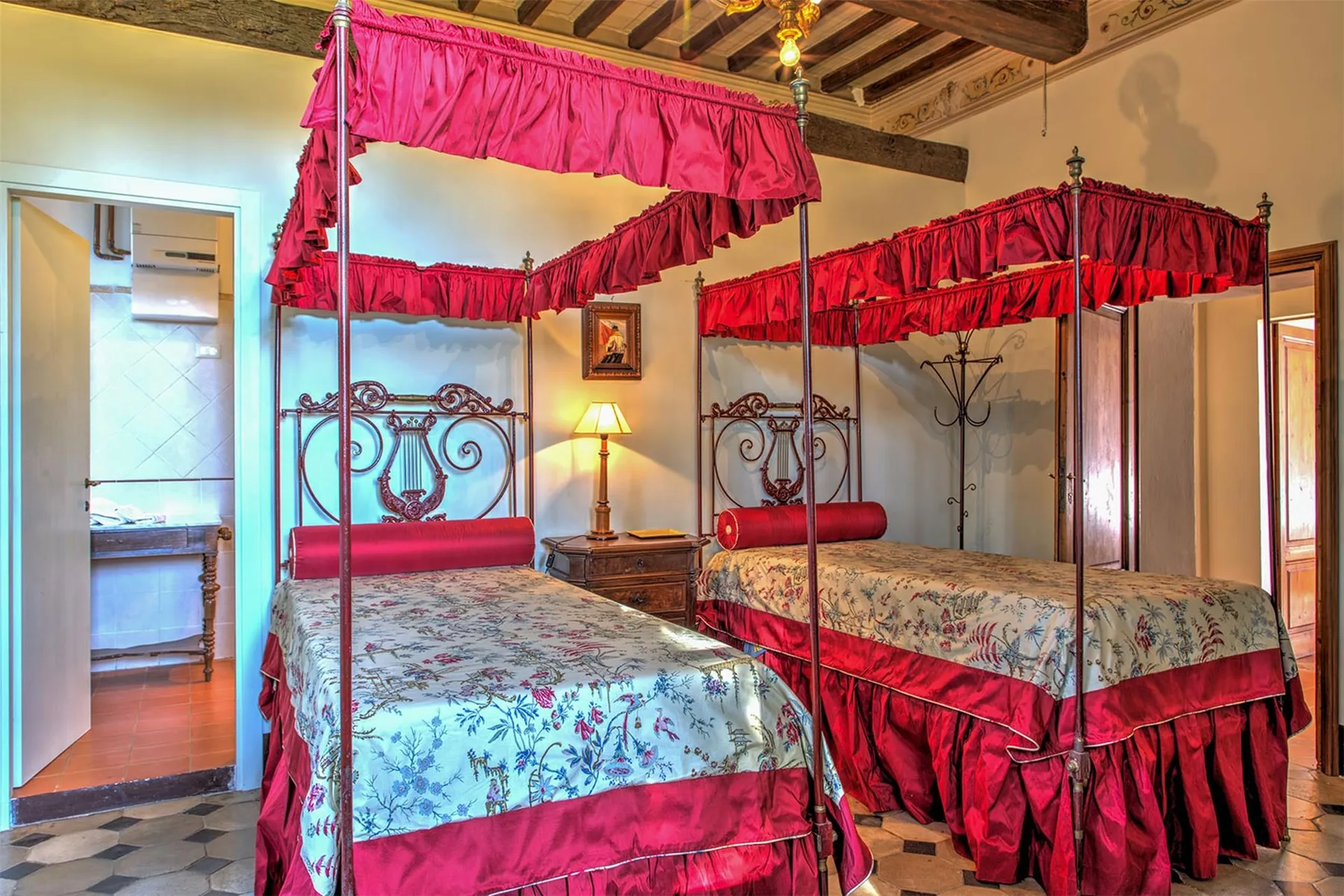 Un dormitorio con dos camas con dosel ornamentadas, cortinas rojas, ropa de cama floral y techo con vigas de madera.