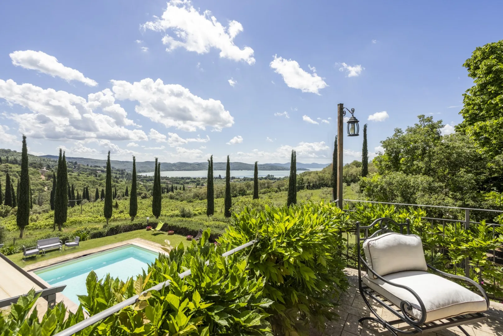 Una terraza soleada da a una piscina y al campo verde, bordeado de altos cipreses.