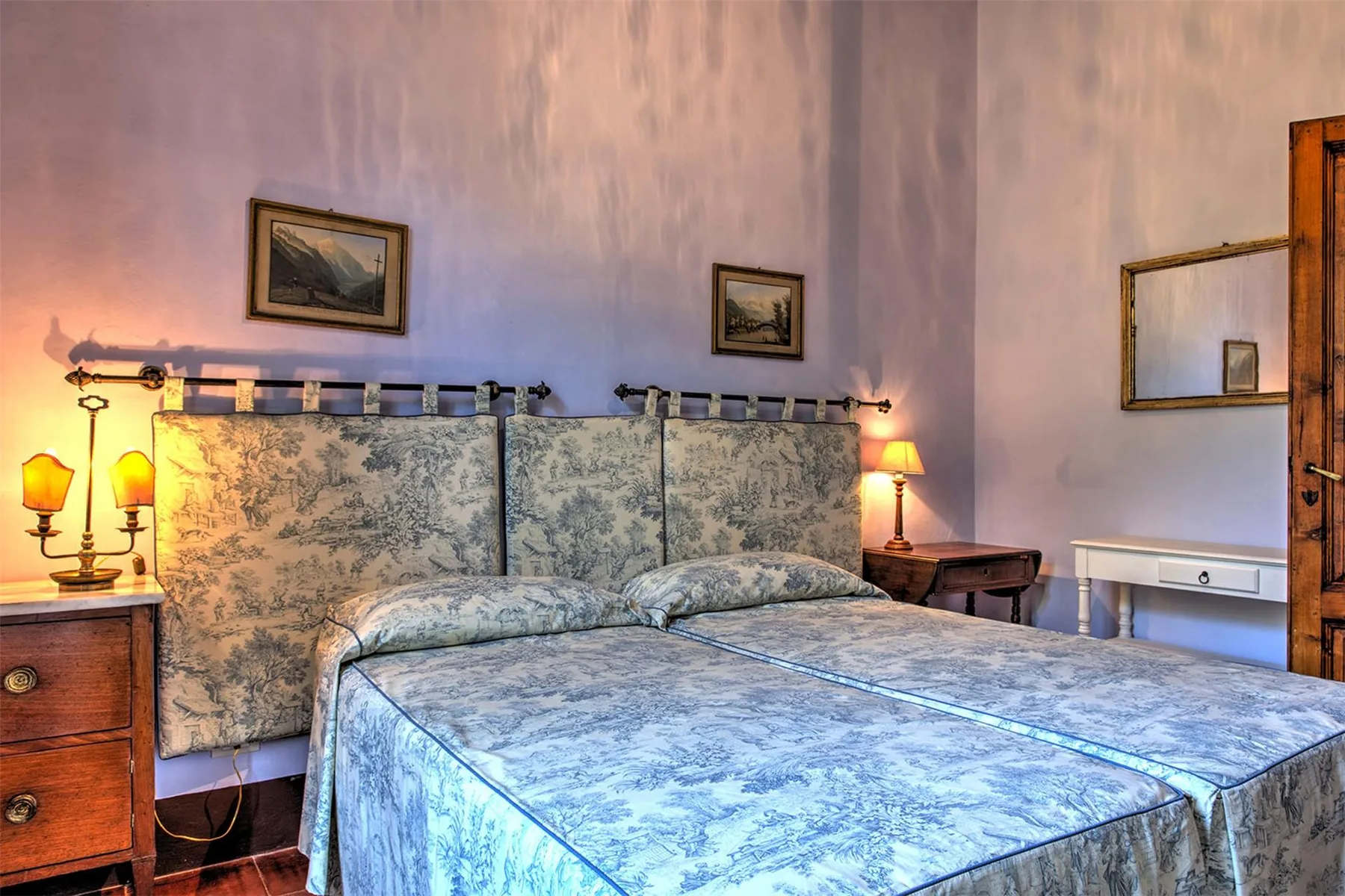 Un dormitorio con una cama grande, ropa de cama azul estampada, un cabecero a juego, mesillas y lámparas.