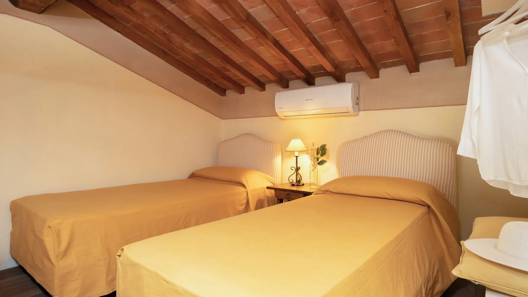 Un dormitorio con dos camas y una lámpara de mesilla bajo un techo inclinado de madera.