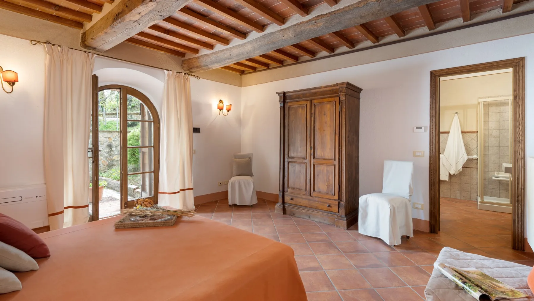 Un dormitorio con una cama cubierta de terracota, un armario de madera y vigas vistas.