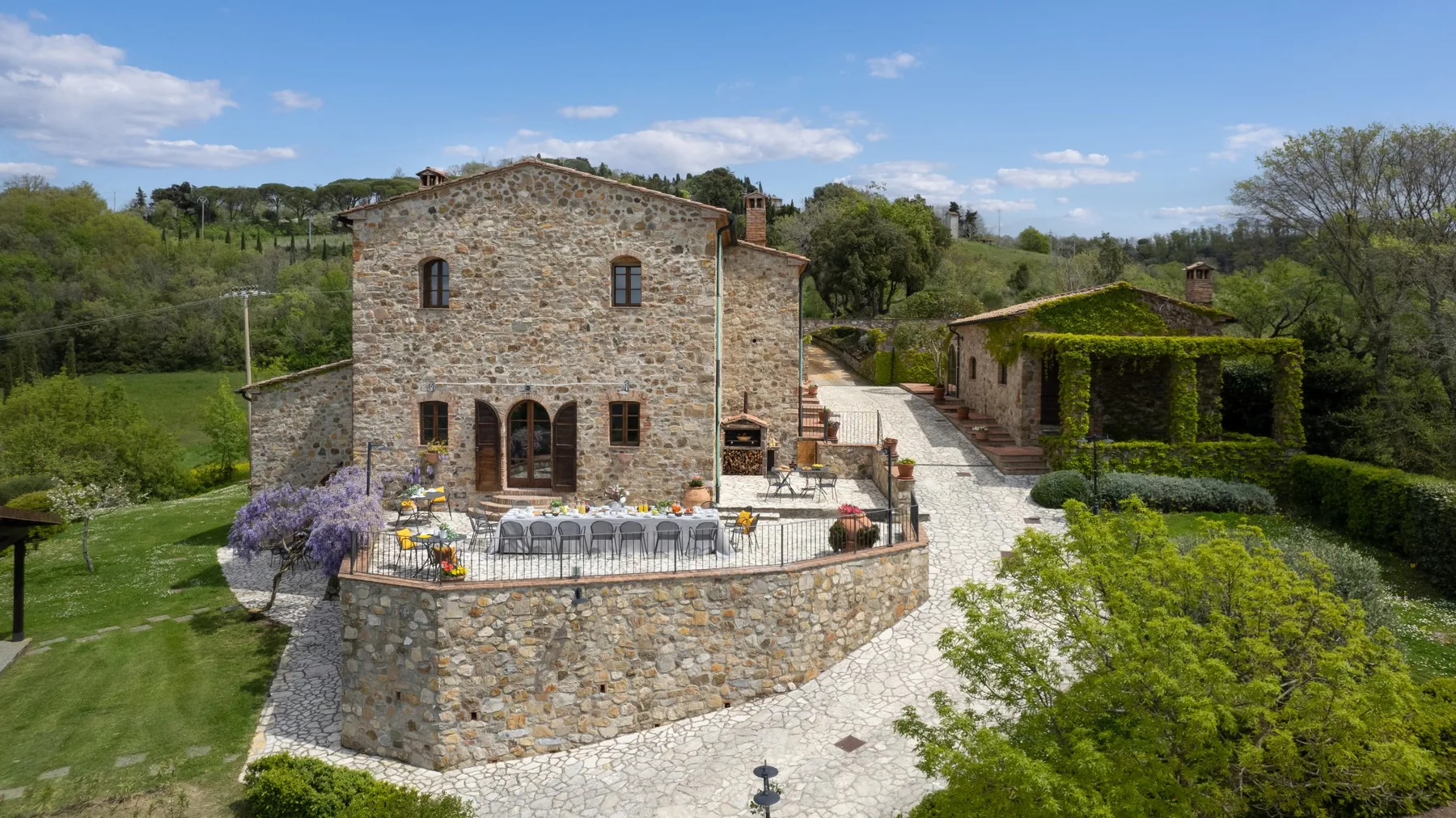 Una casa de piedra y una terraza dan a un jardín verde y un camino curvo de grava.