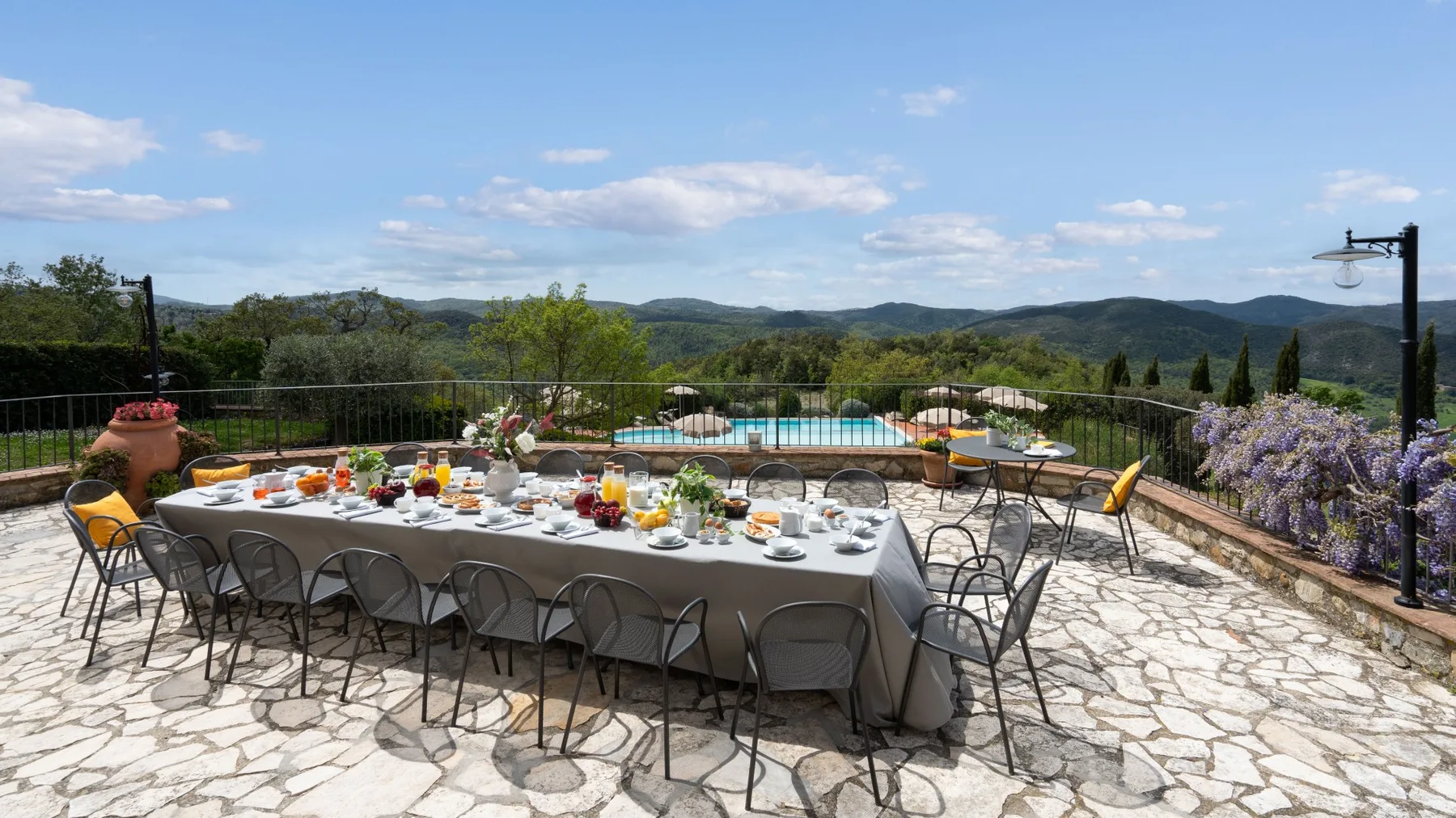 Una terraza exterior con una mesa larga preparada para comer y colinas a lo lejos.