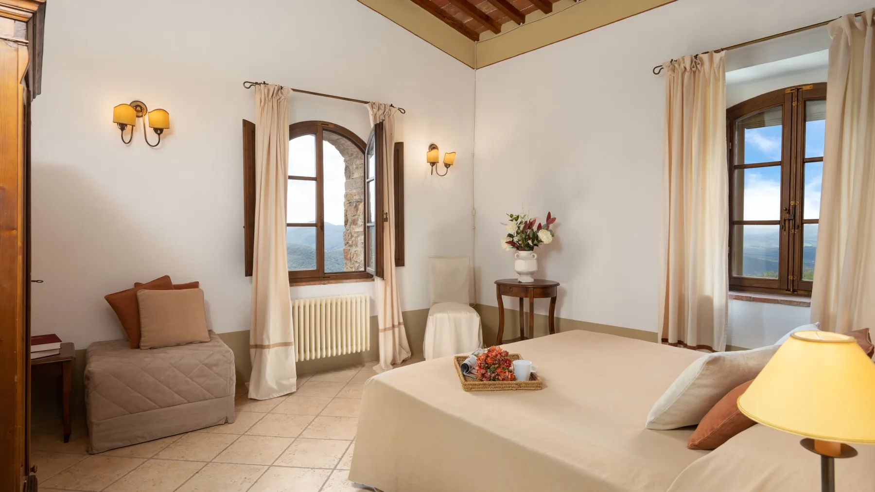 Un dormitorio con una cama grande, ventanas arqueadas y cortinas claras.
