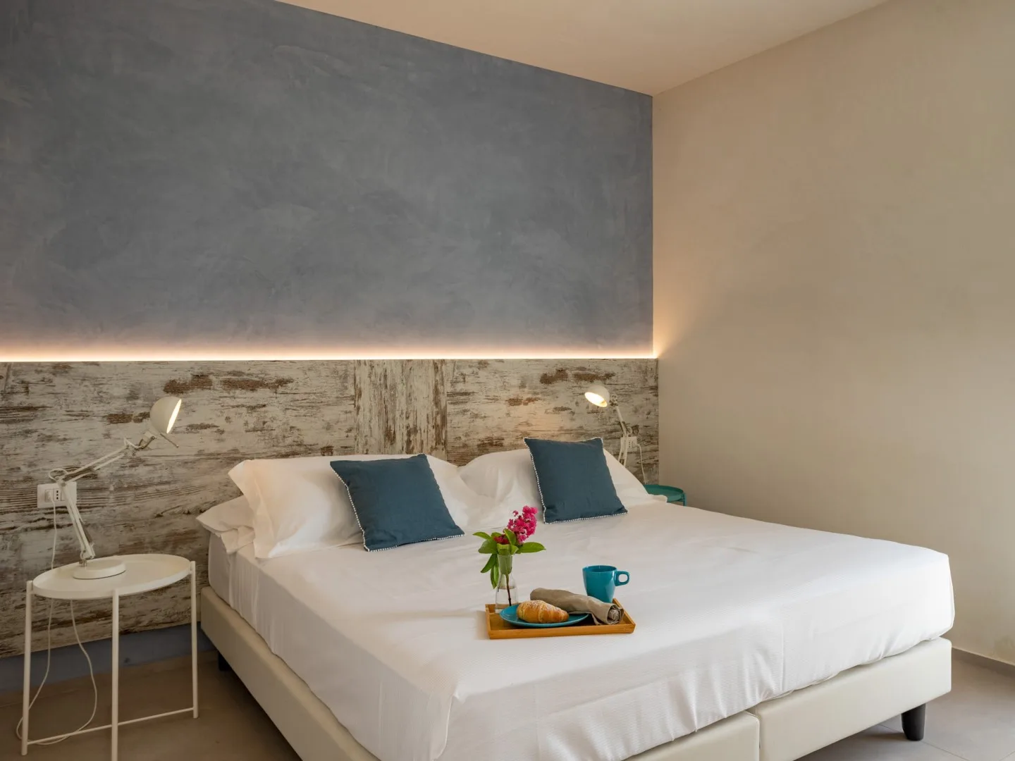 A bedroom with a large bed, blue accent pillows, and a small bedside table.