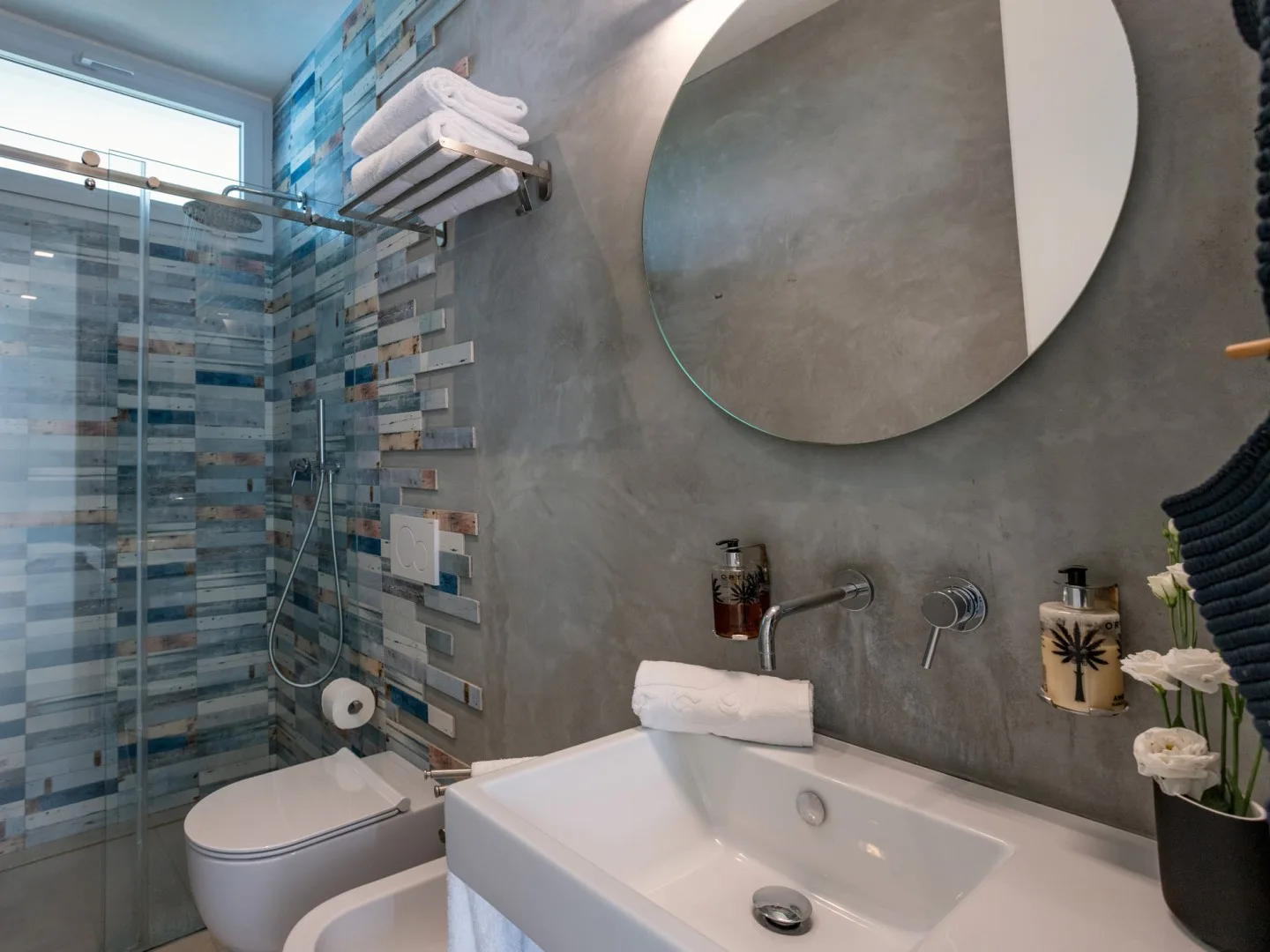 A modern bathroom with a glass shower and a sink beneath a round mirror.