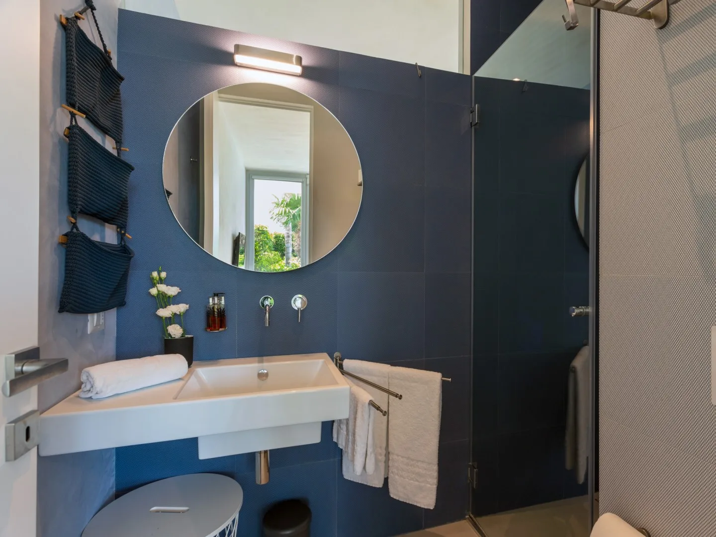 A bathroom vanity with a round mirror and a glass shower.