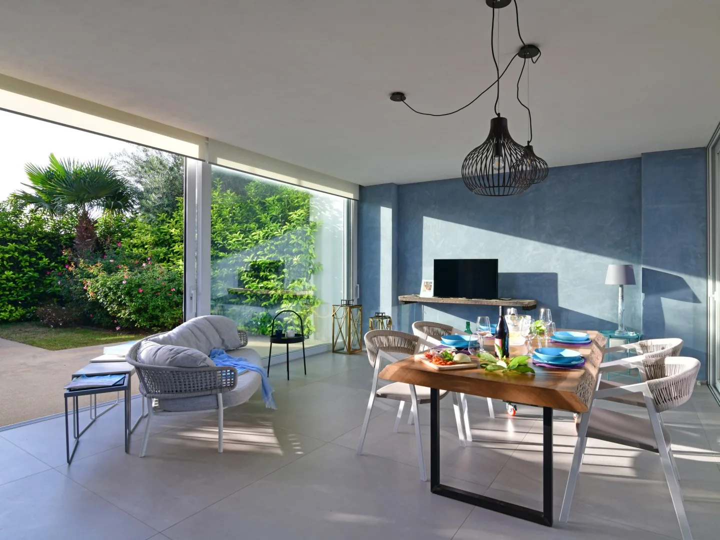 A bright dining and sitting area opens onto a garden through large windows.