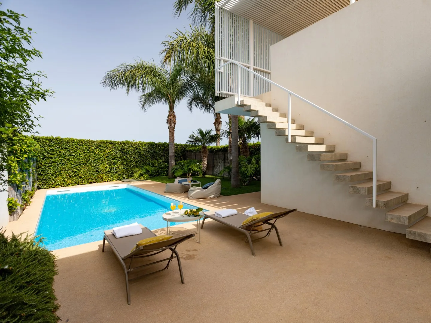 An outdoor pool and adjoining patio with loungers beside a staircase.